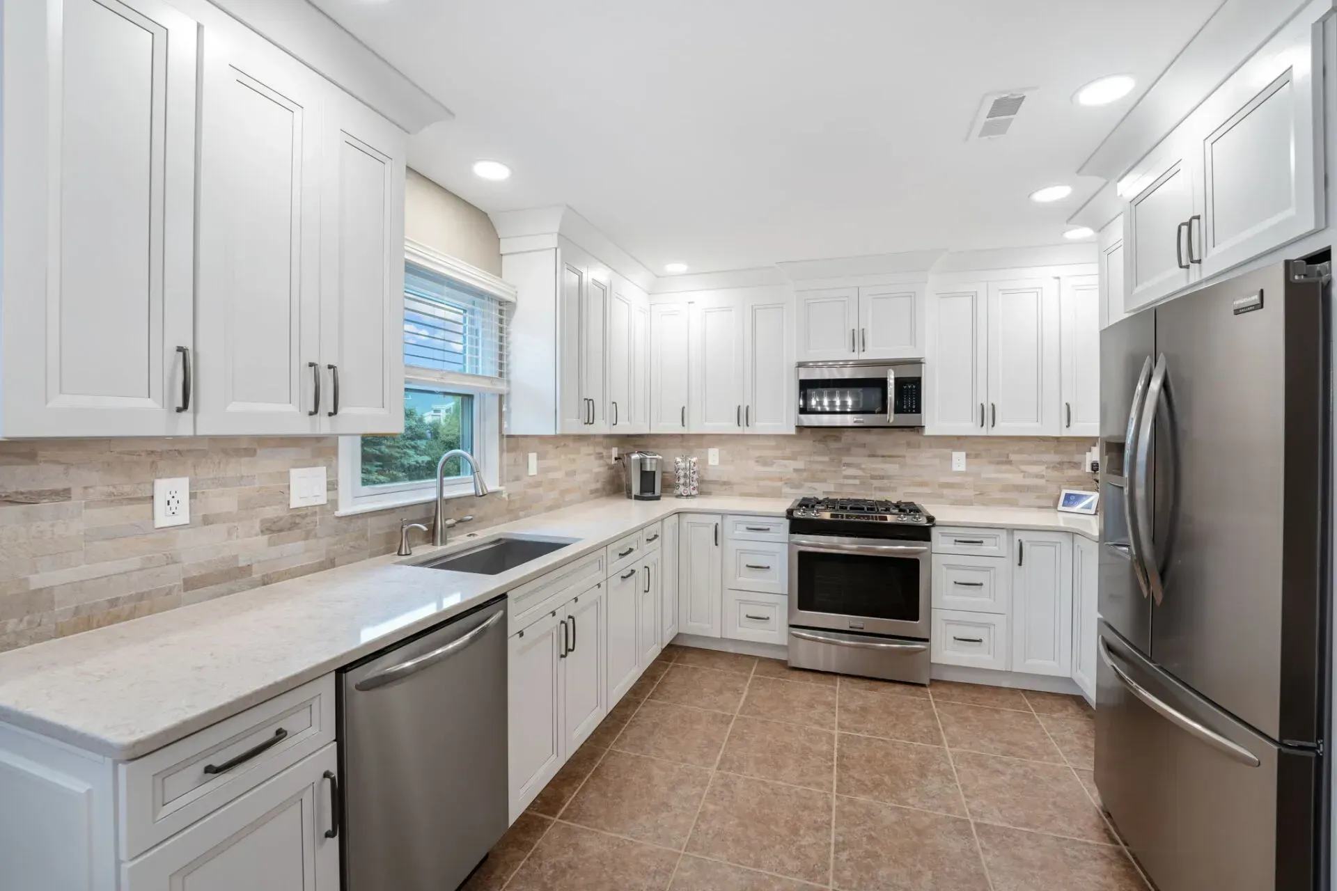 Bright white modern kitchen with stainless steel appliances, beige countertops, and tiled floor  In Bucks County PA
