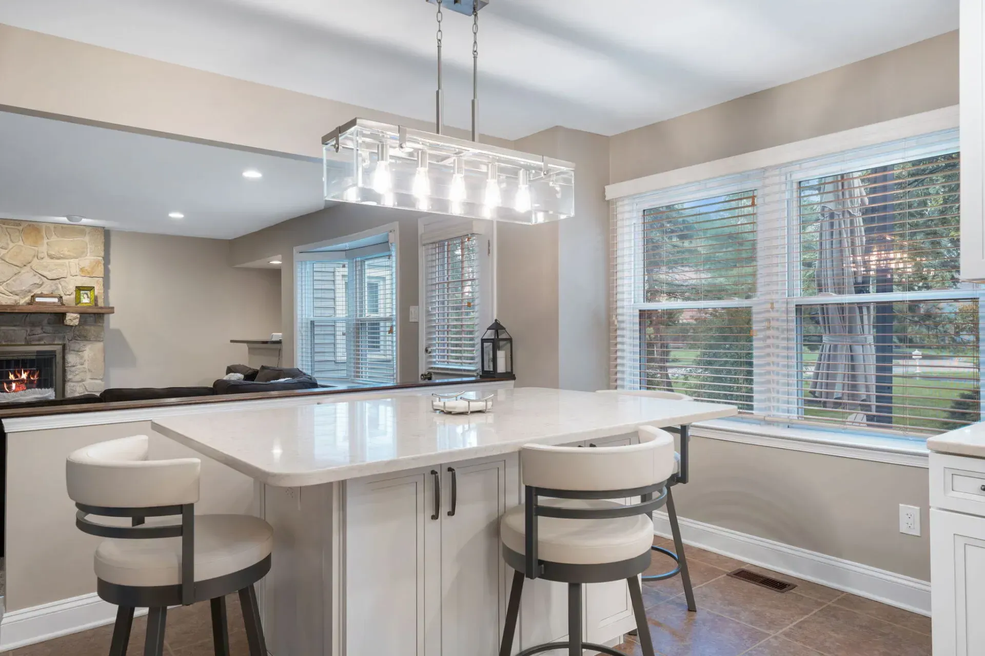 Bright modern kitchen with white island, bar stools, pendant light, and large window seating area In Bucks Country PA