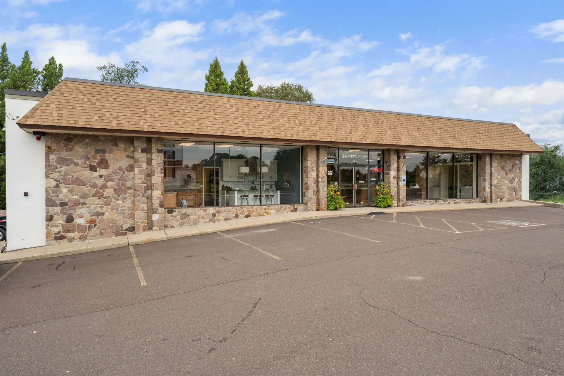 Single-story stone storefront with large windows and a tan shingle roof beside an empty parking lot  In Bucks County PA