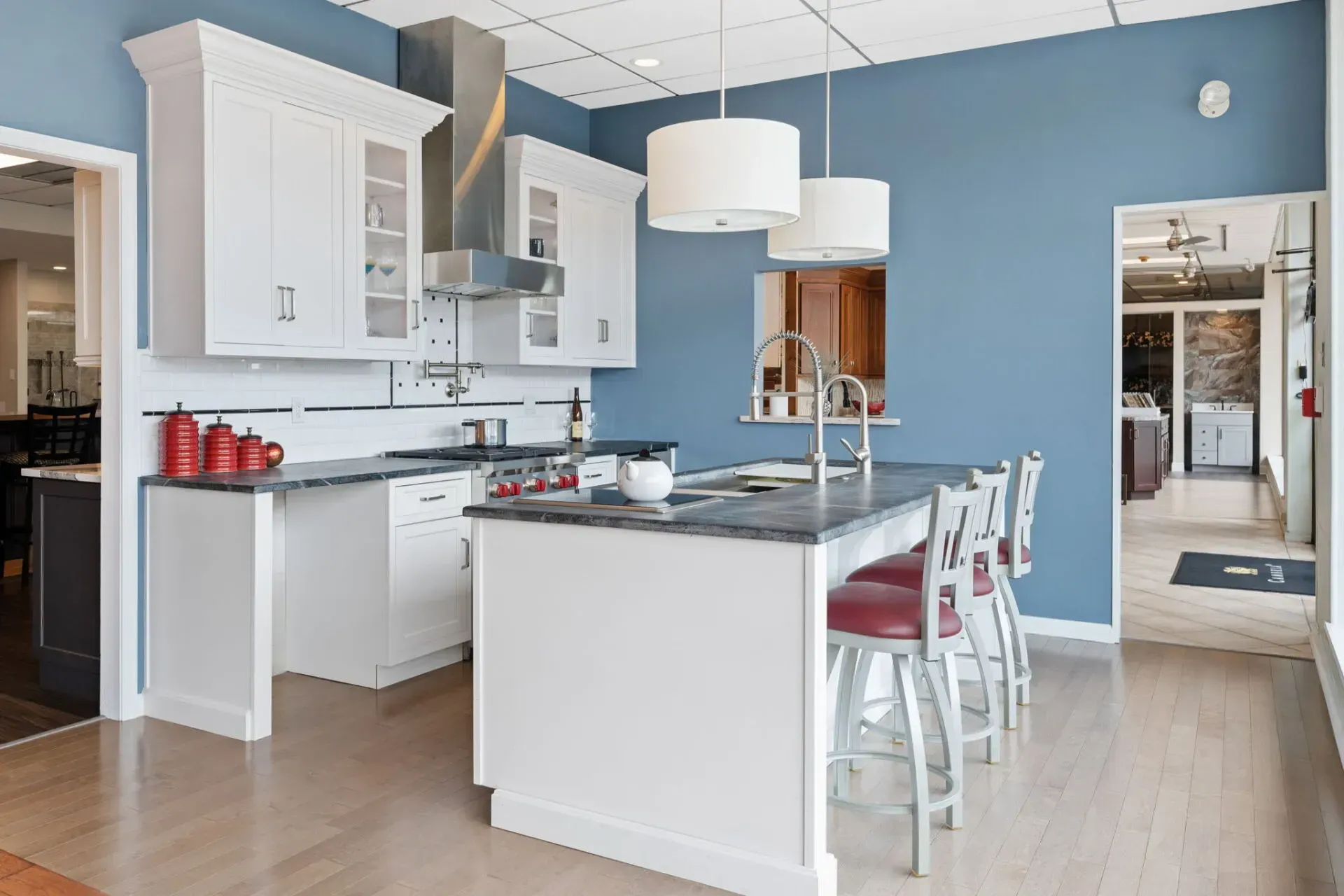 Bright blue kitchen with white cabinets, island, pendant lights, and a dining table beside a doorway  In Bucks County PA