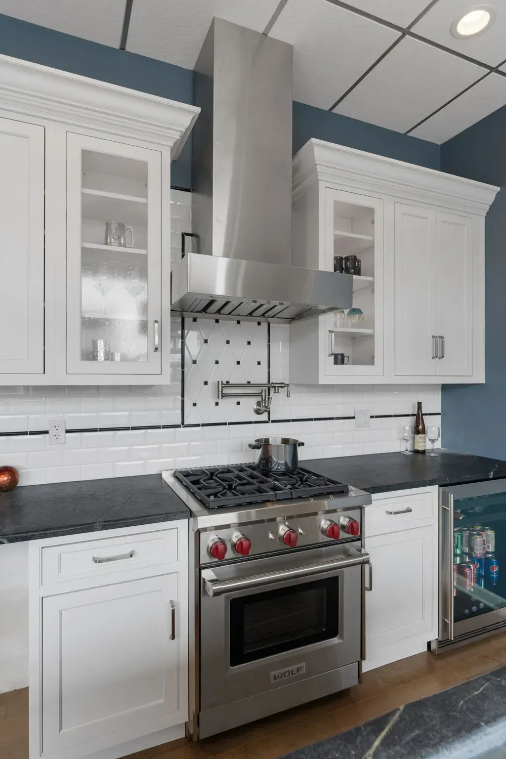 Modern white kitchen with stainless steel range, hood, and glass-front cabinets  In Bucks County PA