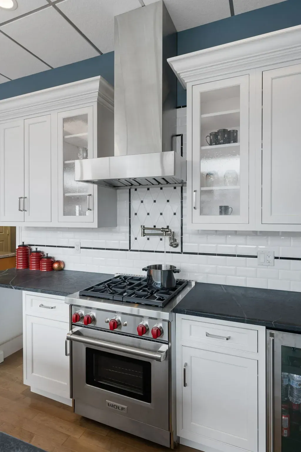 Modern white kitchen with stainless steel stove, black countertops, and glass-front cabinets  In Bucks County PA