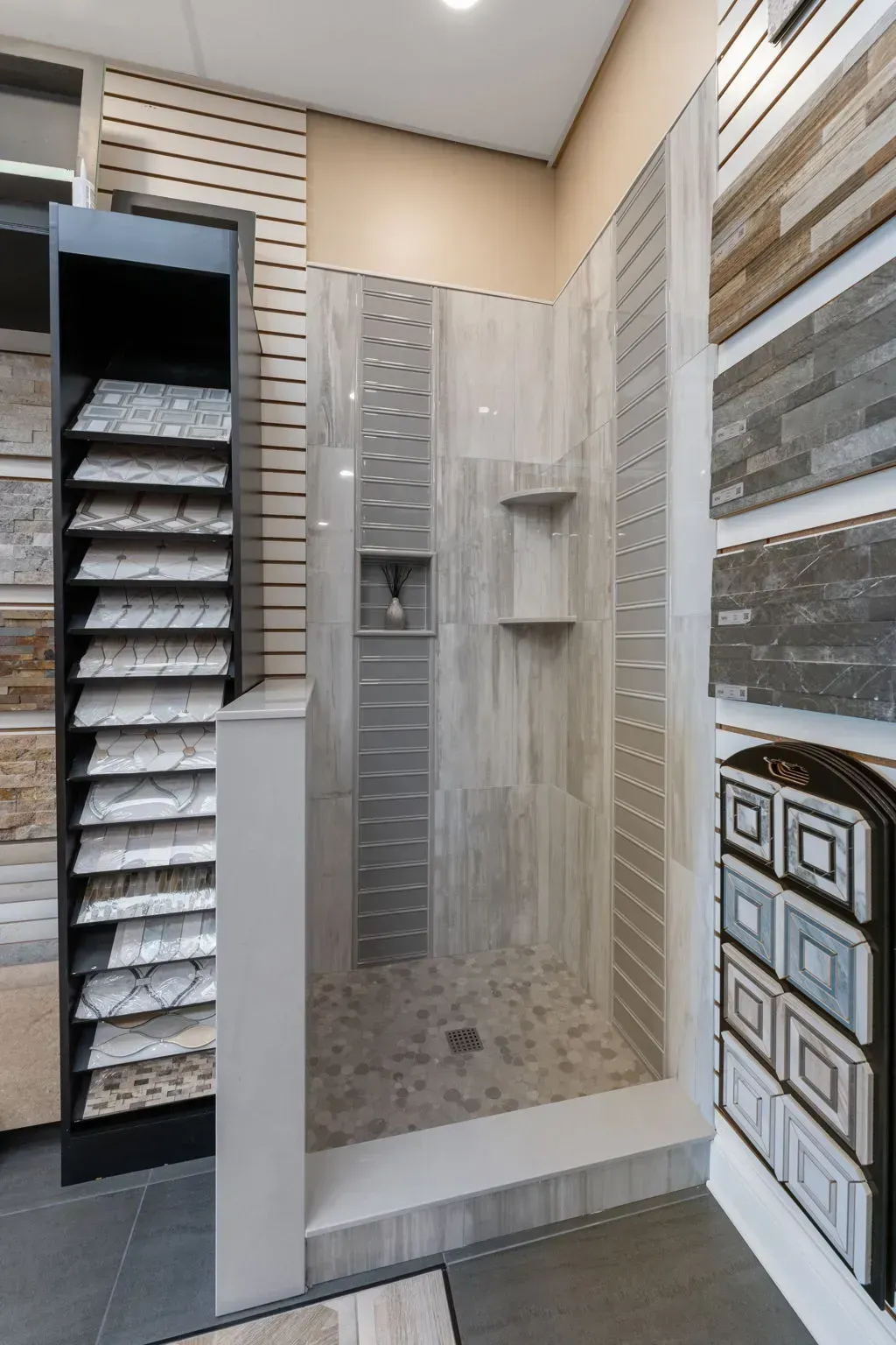 Showroom shower display with beige and gray tile, glass enclosure, and sample shelves nearby  In Bucks County PA