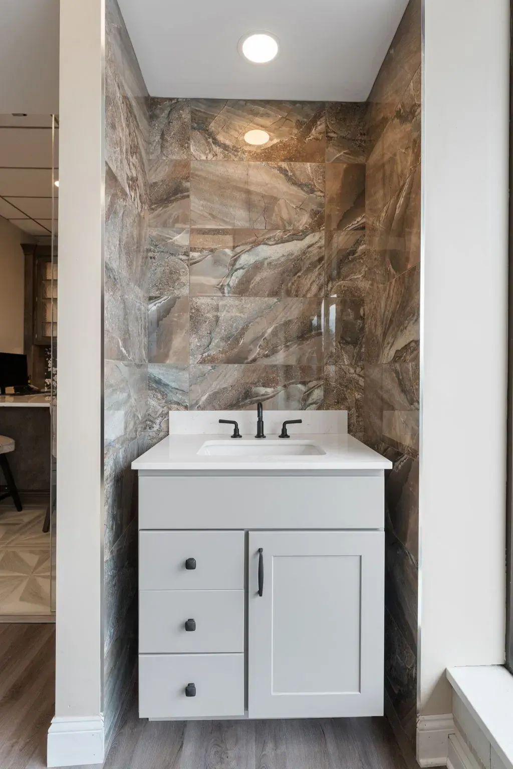 Small white bathroom vanity with sink and mirror in a tiled alcove, lit by recessed ceiling light  In Bucks County PA