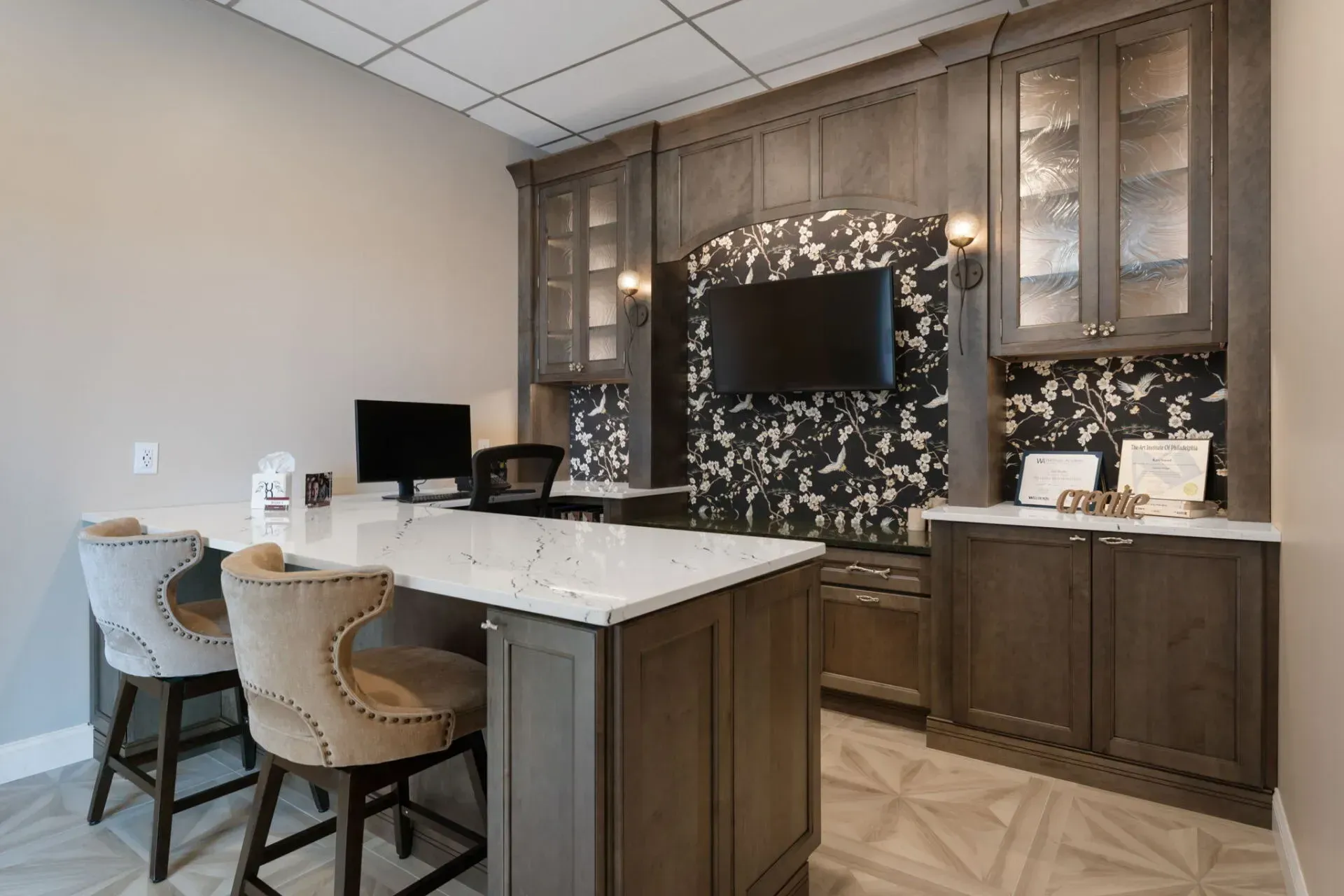 Modern kitchen bar with two woven chairs, white countertop, dark wood cabinets, and a TV mounted on the wall  In Bucks County PA