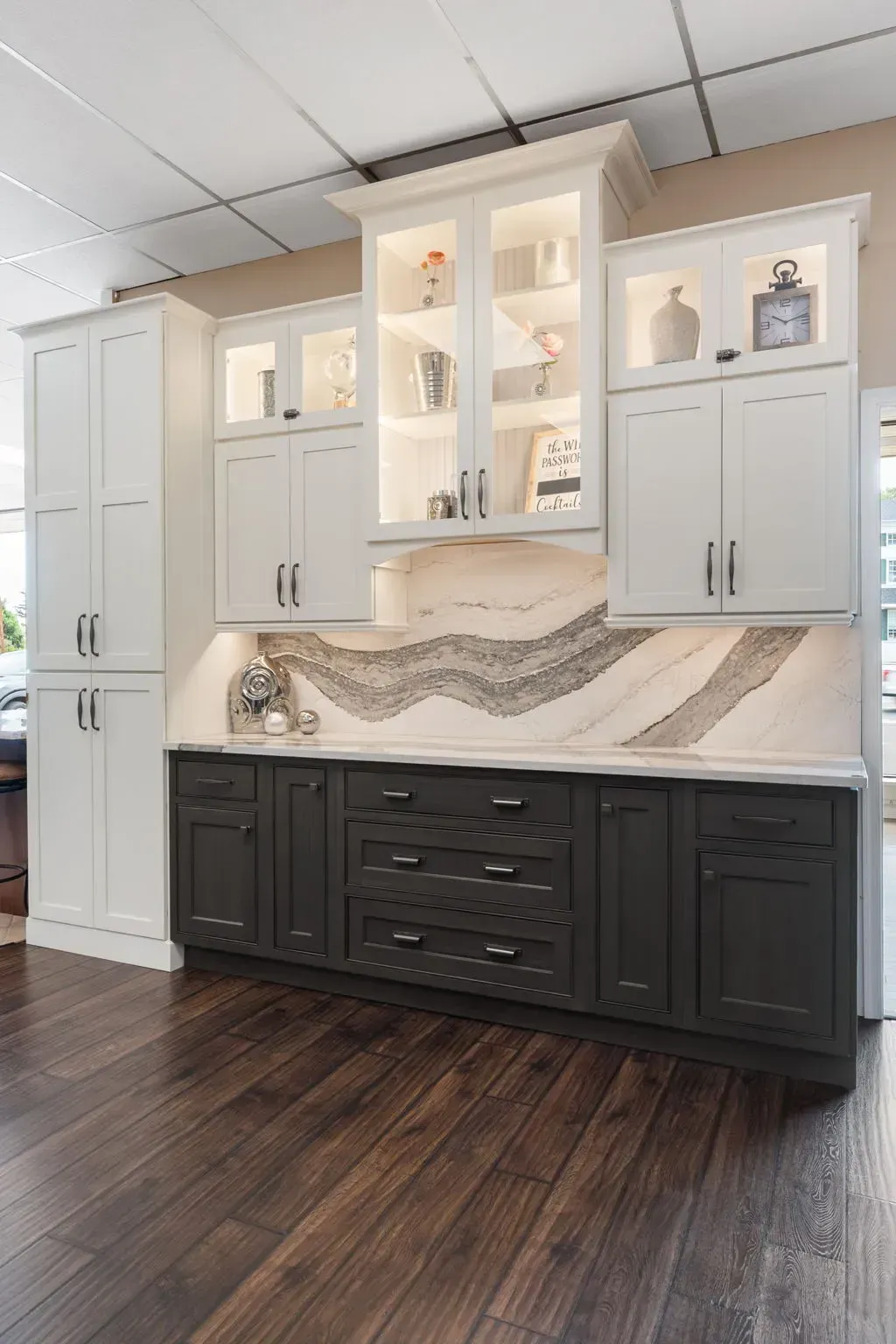 White and dark-gray kitchen cabinets with glass display doors, tiled backsplash, and dark wood floor  In Bucks County PA