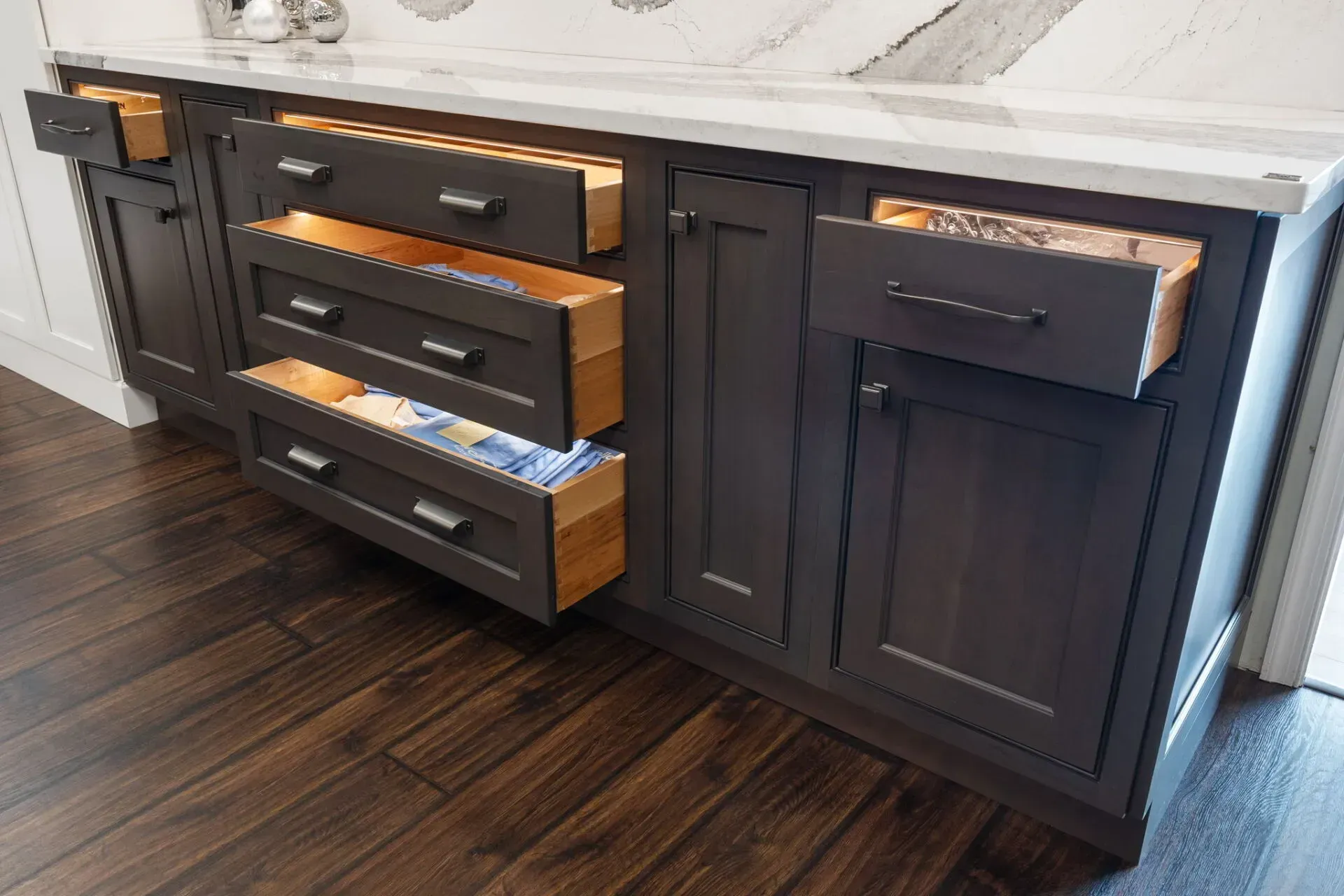 Dark wood kitchen cabinet with three open drawers beside a sink and countertop, on a hardwood floor  In Bucks County PA