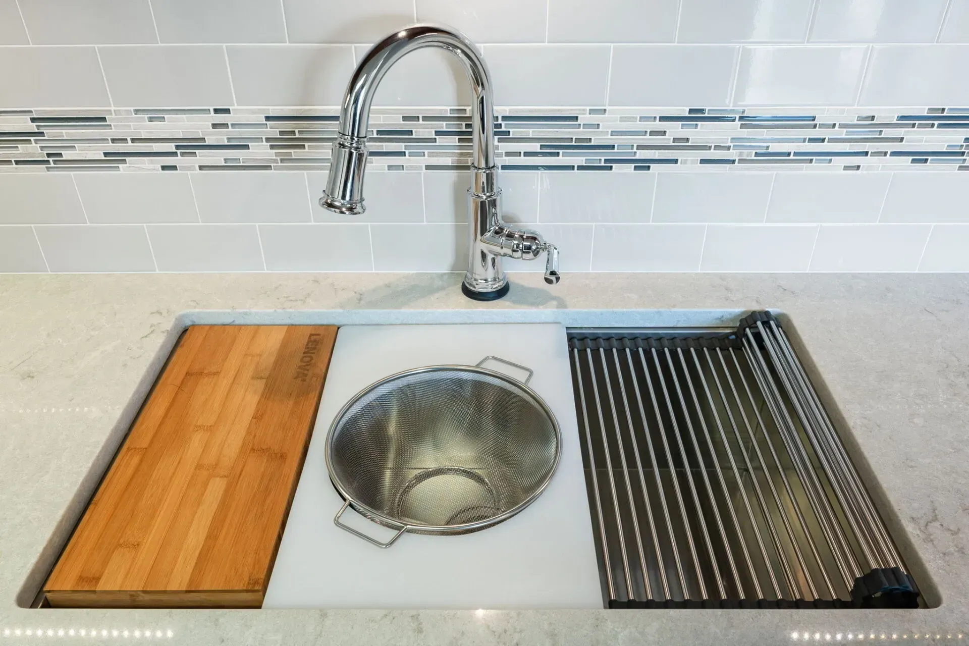 Kitchen sink with farmhouse basin, chrome faucet, wood cutting board, and drying rack insert on a gray counter  In Bucks County PA