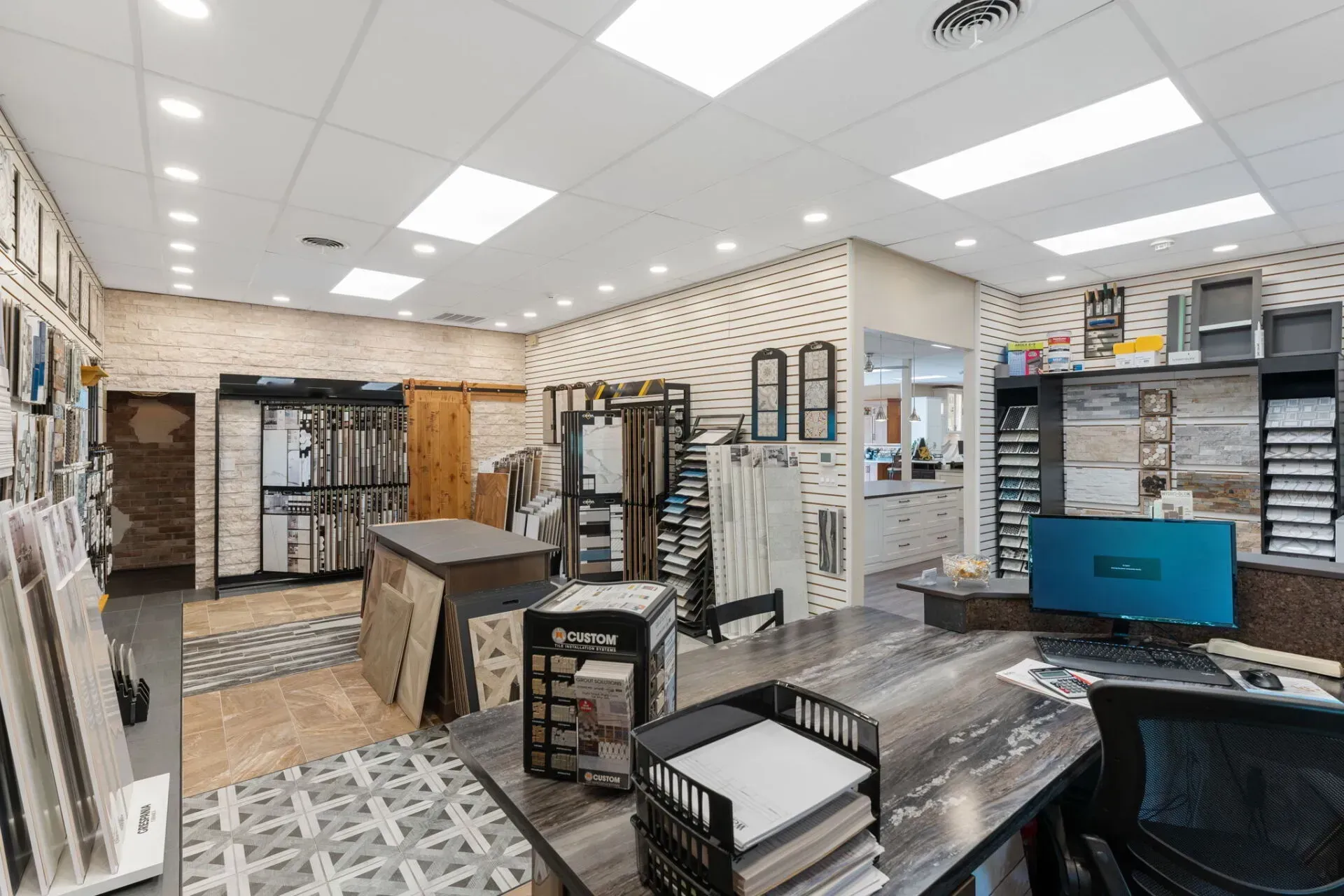 Bright tile showroom with flooring samples, display racks, and a counter under recessed ceiling lights  In Bucks County PA