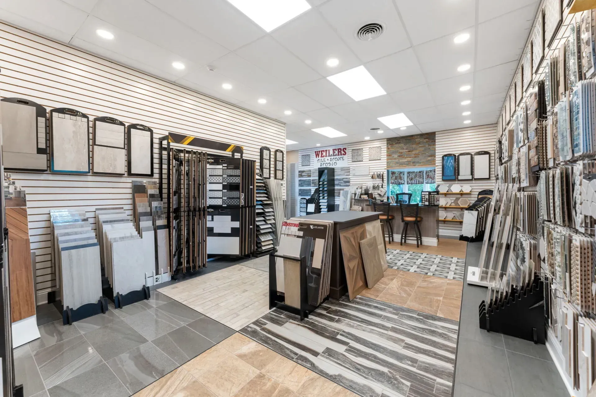 Carpet and flooring showroom with display racks, sample boards, and patterned rugs under bright ceiling lights  In Bucks County PA