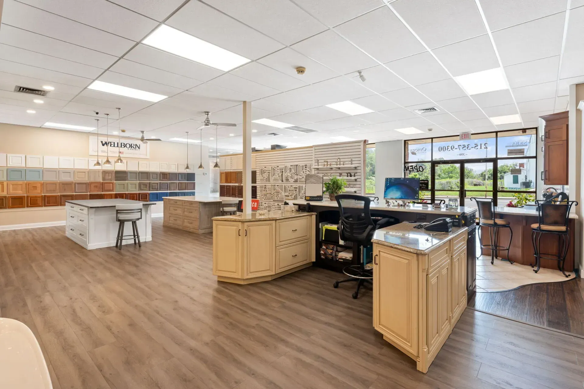 Bright kitchen showroom with white ceiling lights, wooden floors, cabinets, and display islands near large windows In Bucks Country PA