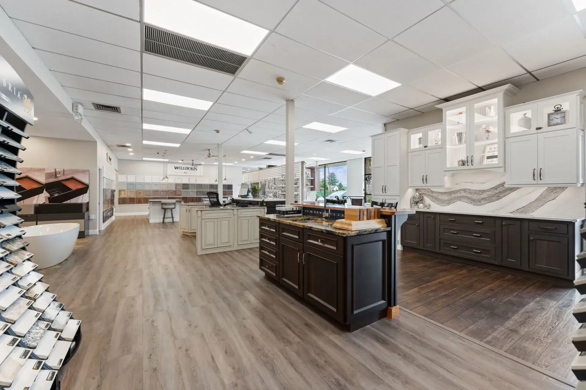 Bright kitchen showroom with white cabinets, dark wood islands, and wood-look flooring  In Bucks County PA