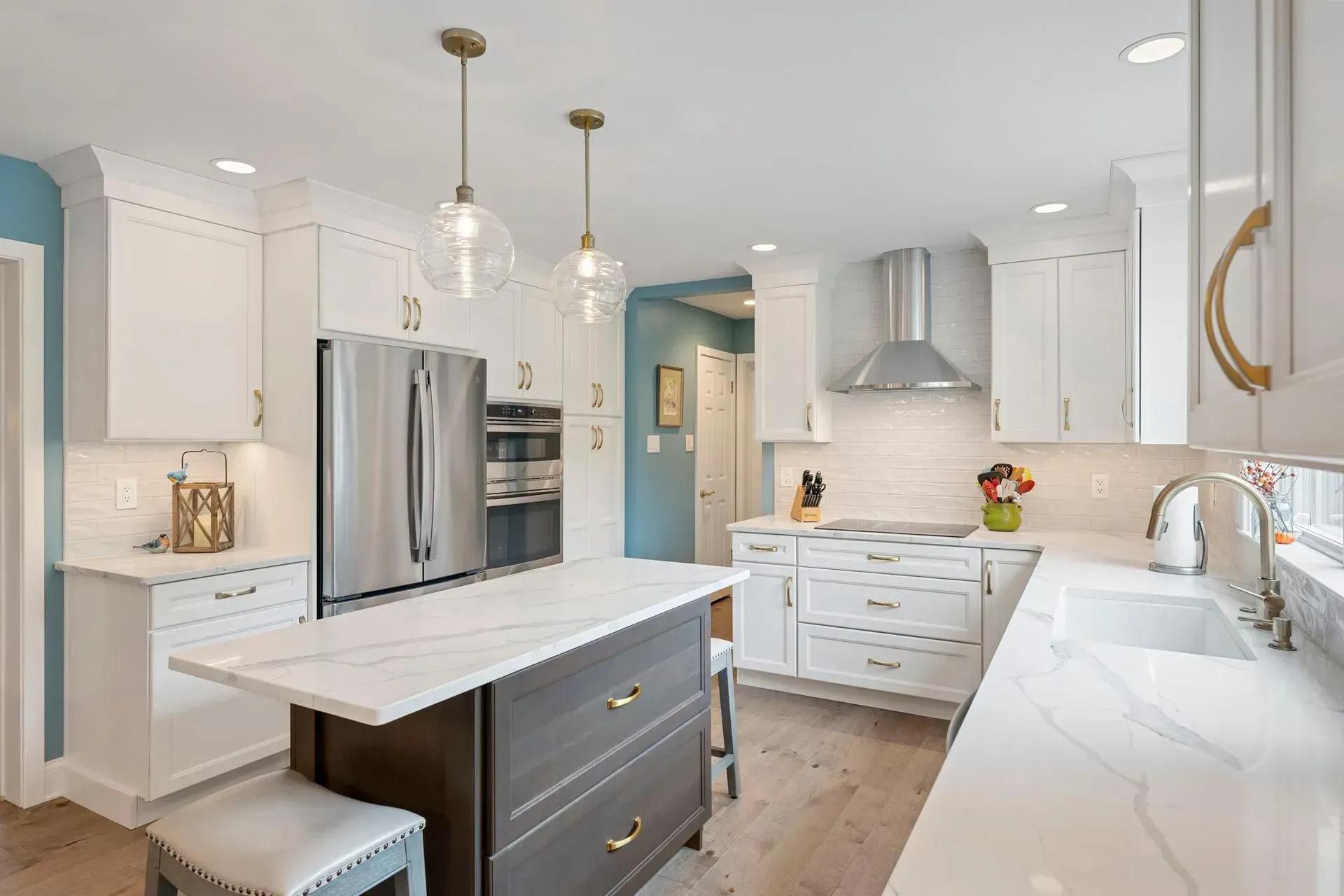Bright modern kitchen with white cabinets, stainless fridge, marble island, and pendant lights  In Bucks County PA