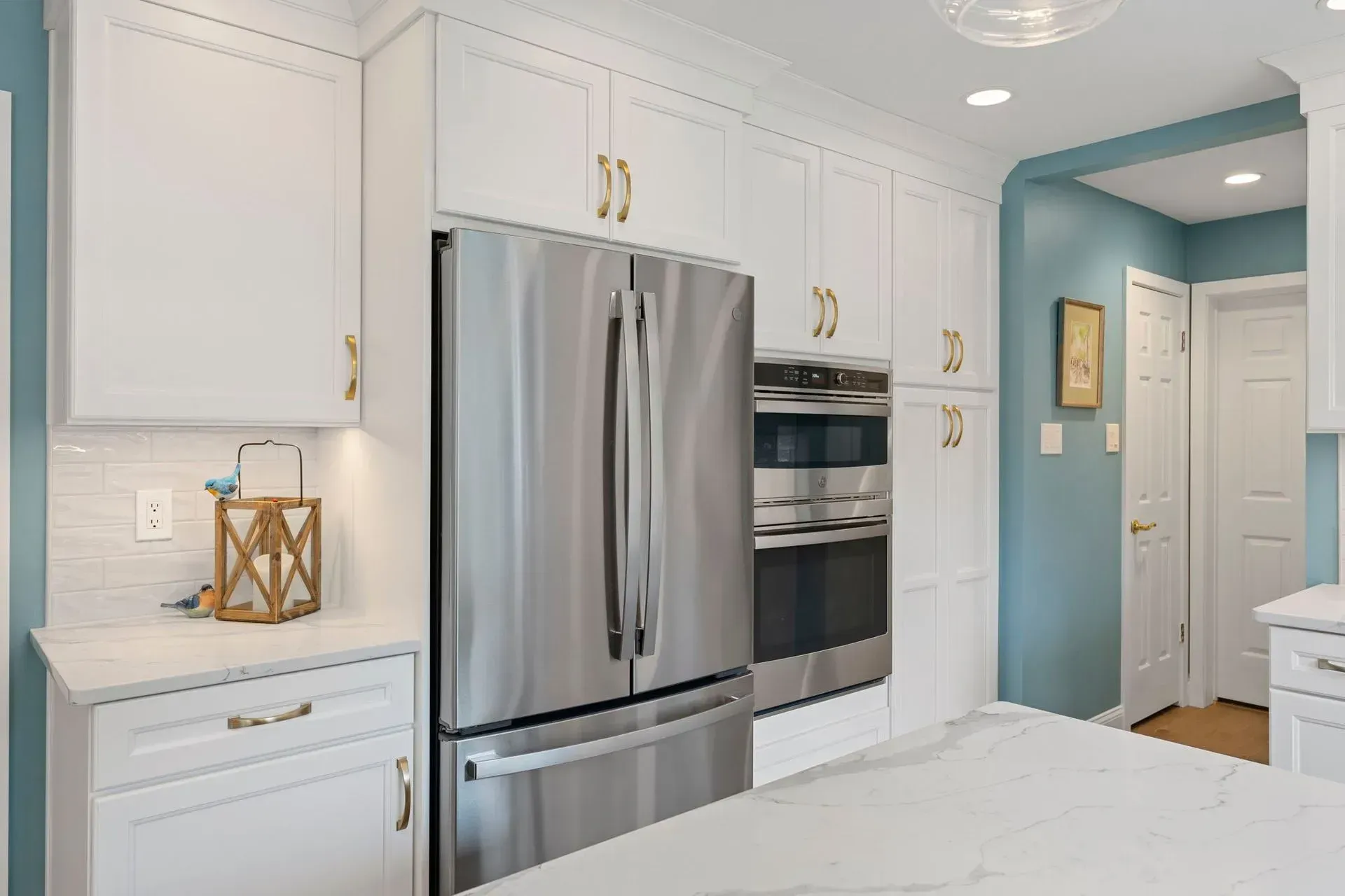 Bright white kitchen with stainless steel refrigerator, built-in oven, and blue hallway in background  In Bucks County PA