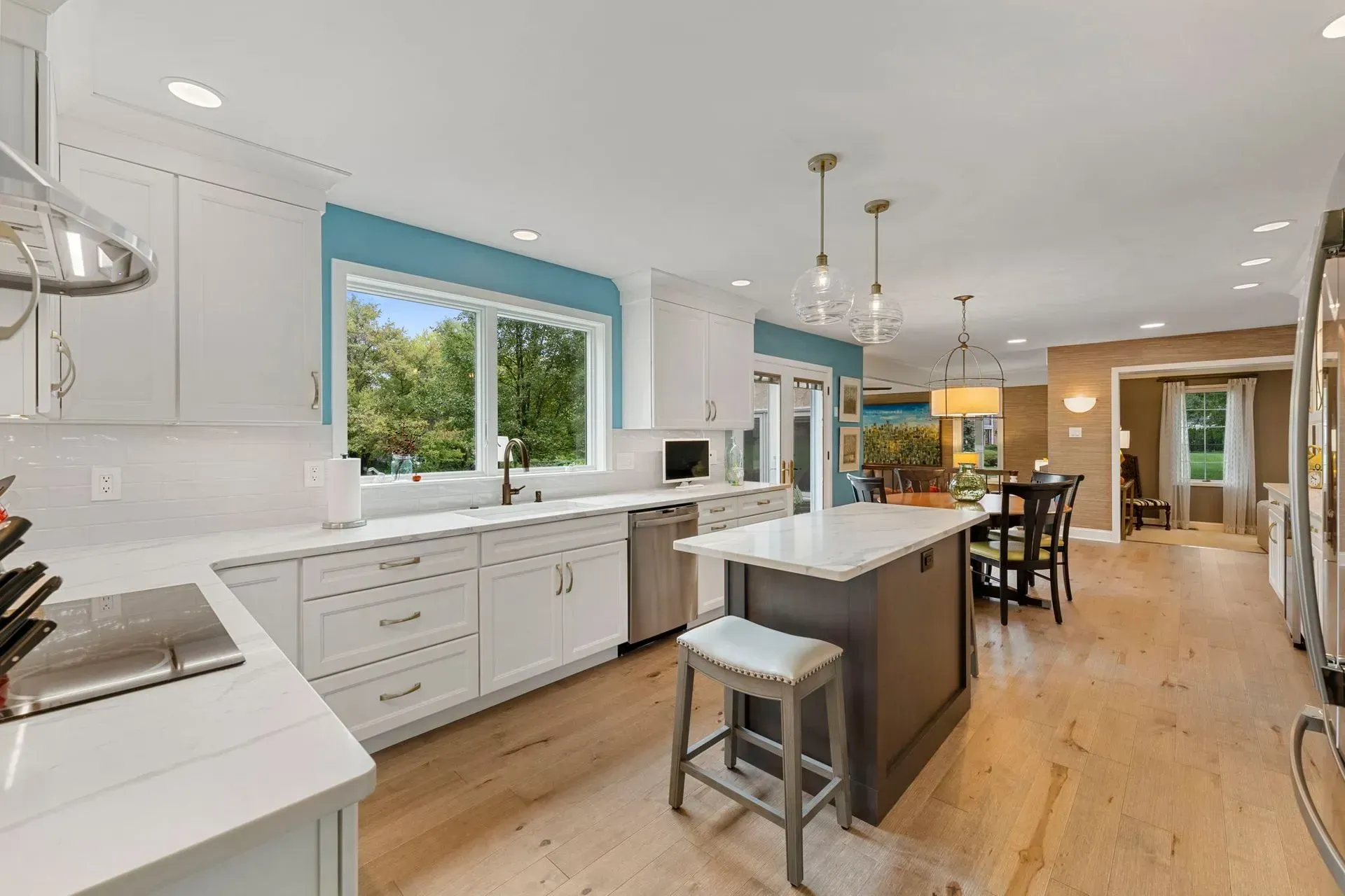 Bright modern kitchen with white cabinets, large island, wood floors, and blue-trimmed window overlooking a dining area  In Bucks County PA