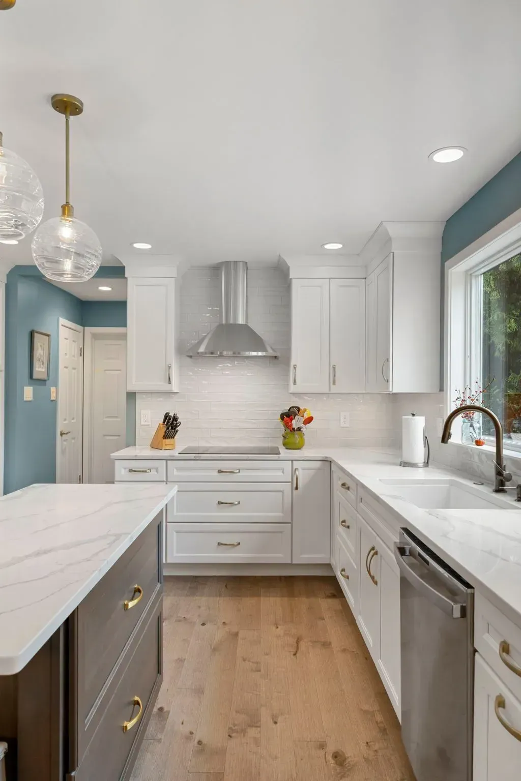 Bright modern white kitchen with marble island, pendant lights, stainless range hood, and wood floor  In Bucks County PA
