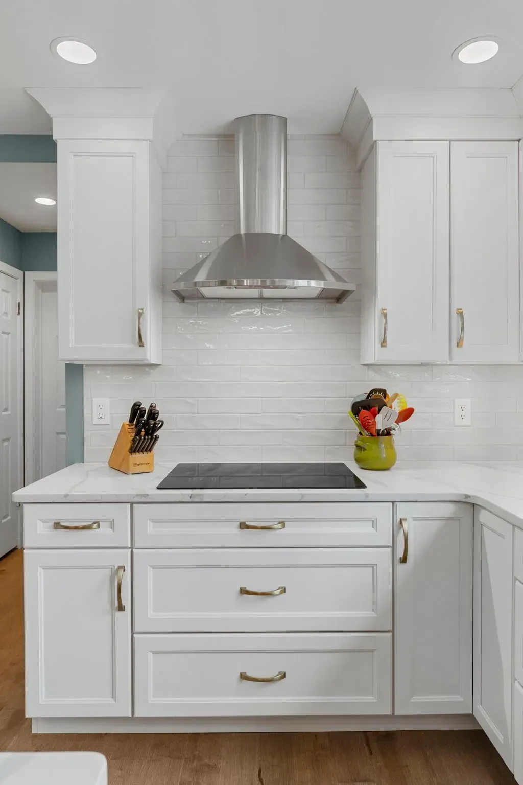 Bright white kitchen with stainless range hood, gray cooktop, white cabinets, and countertop decor  In Bucks County PA