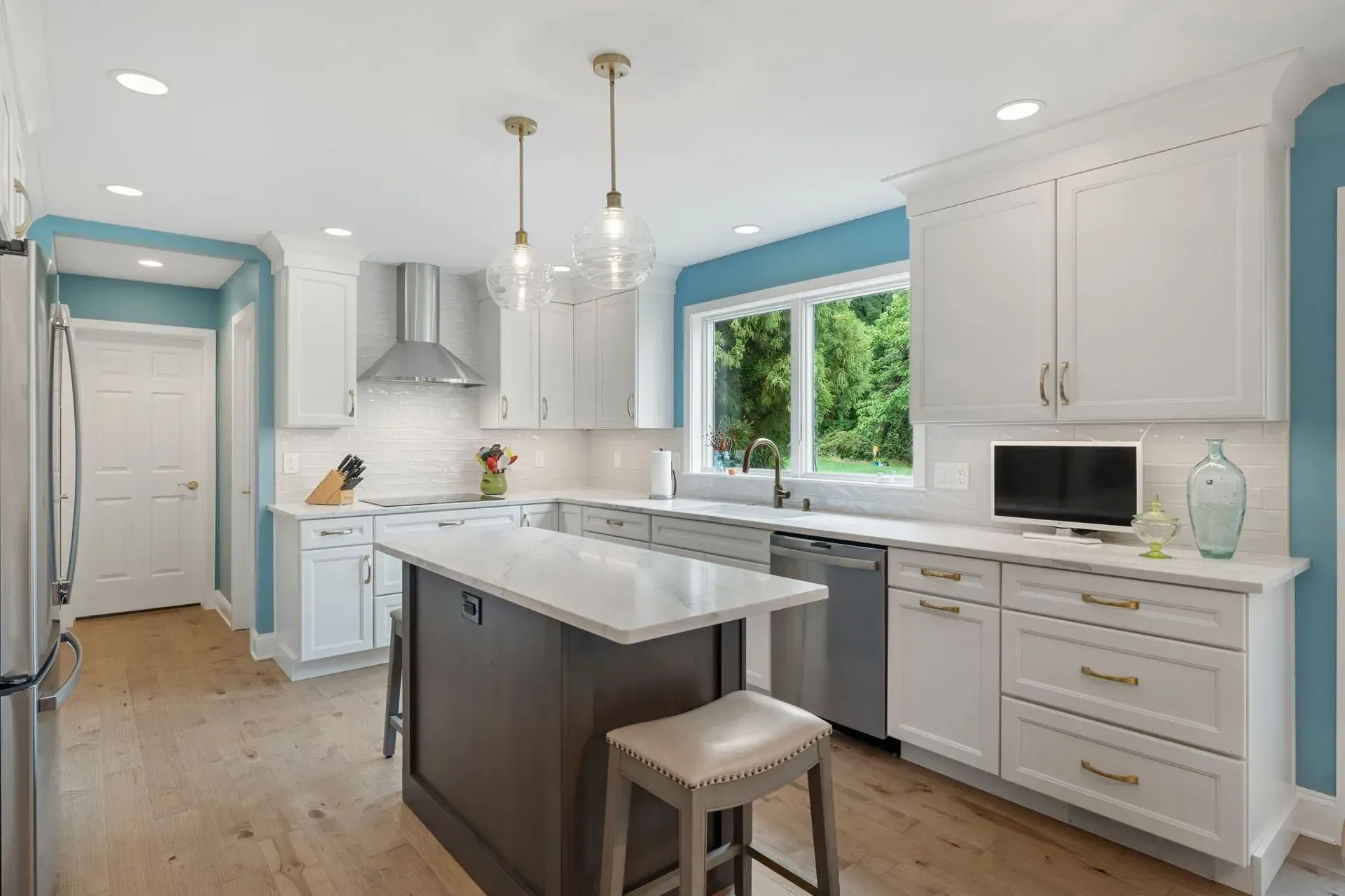 Bright white kitchen with island, stainless hood, blue walls, and large window In Bucks Country PA