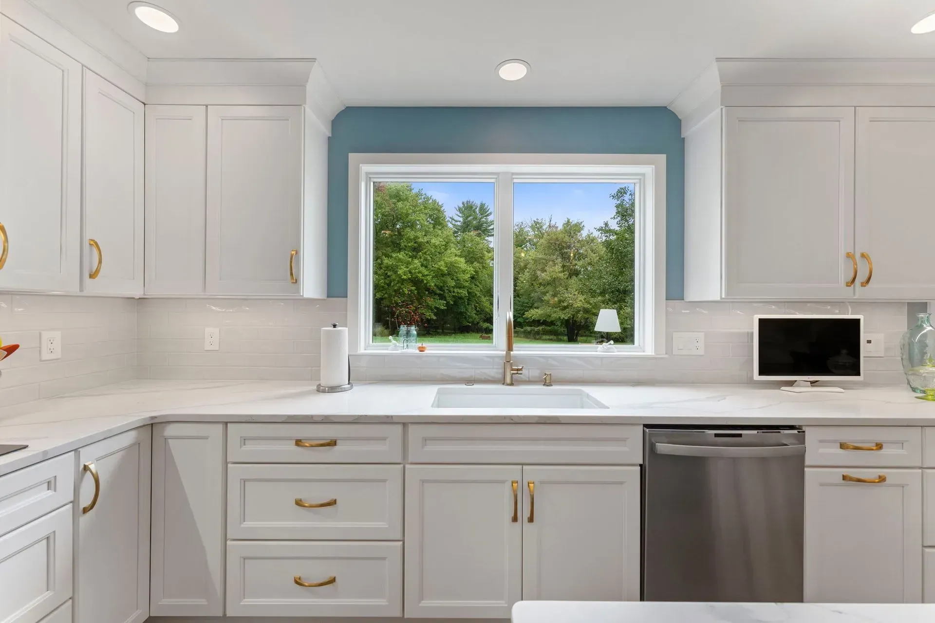 Bright white kitchen with gold hardware, stainless dishwasher, and a window over the sink  In Bucks County PA