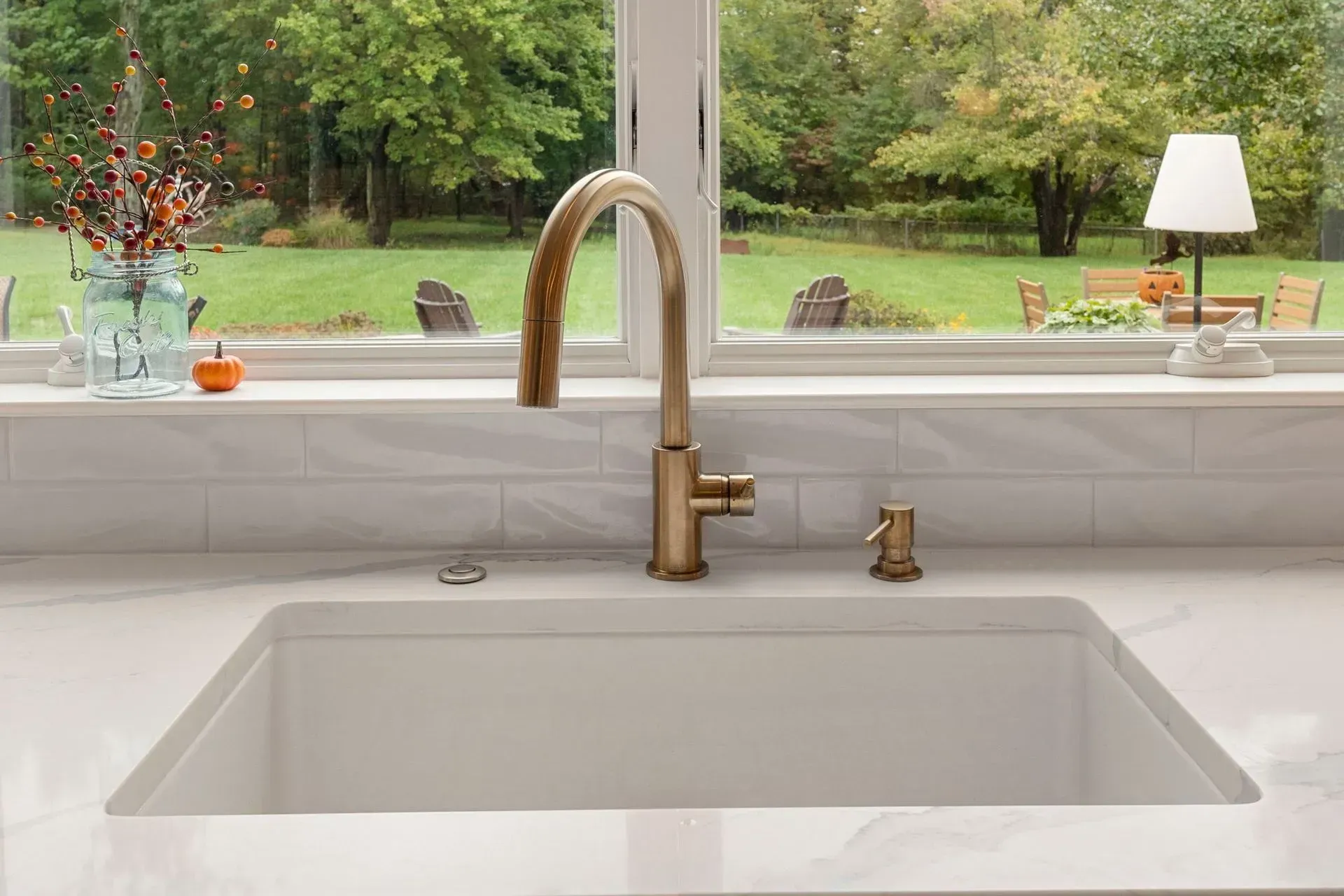 Kitchen sink with brass faucet beneath a window overlooking a green backyard  In Bucks County PA