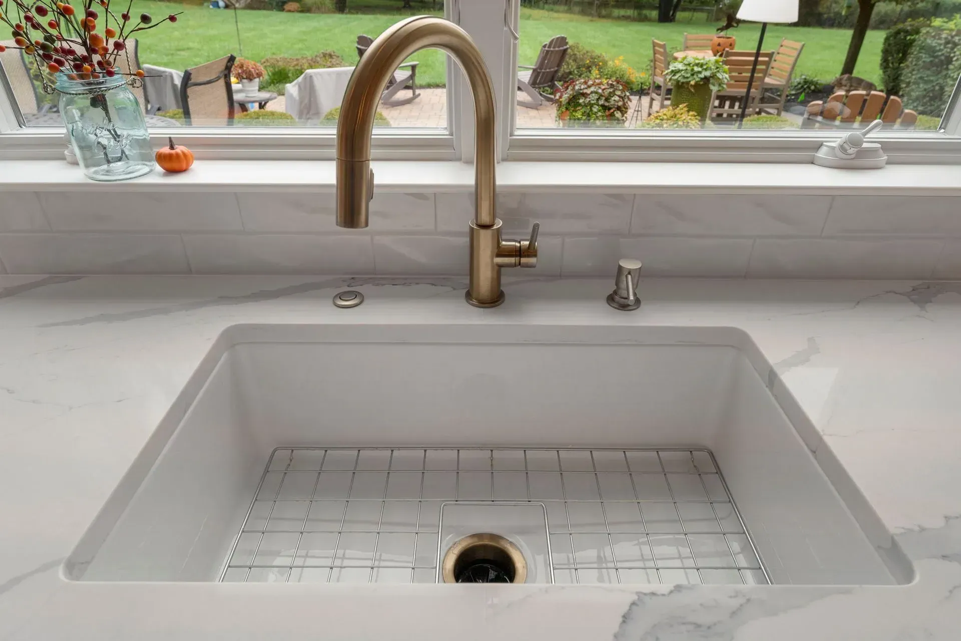 Modern white kitchen sink with brass faucet and garden view through the window  In Bucks County PA