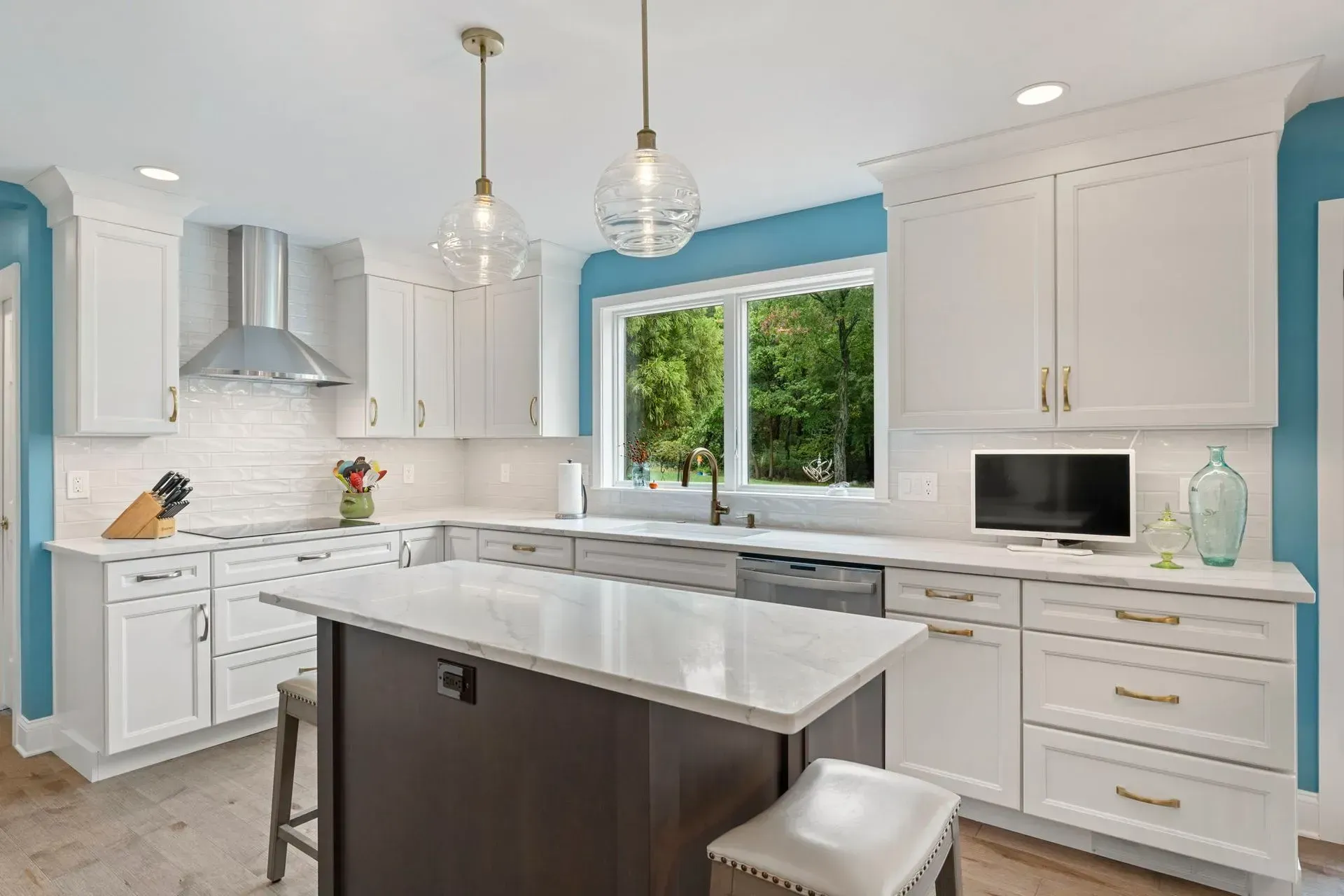 Bright modern white kitchen with marble island, pendant lights, and a large window overlooking greenery  In Bucks County PA