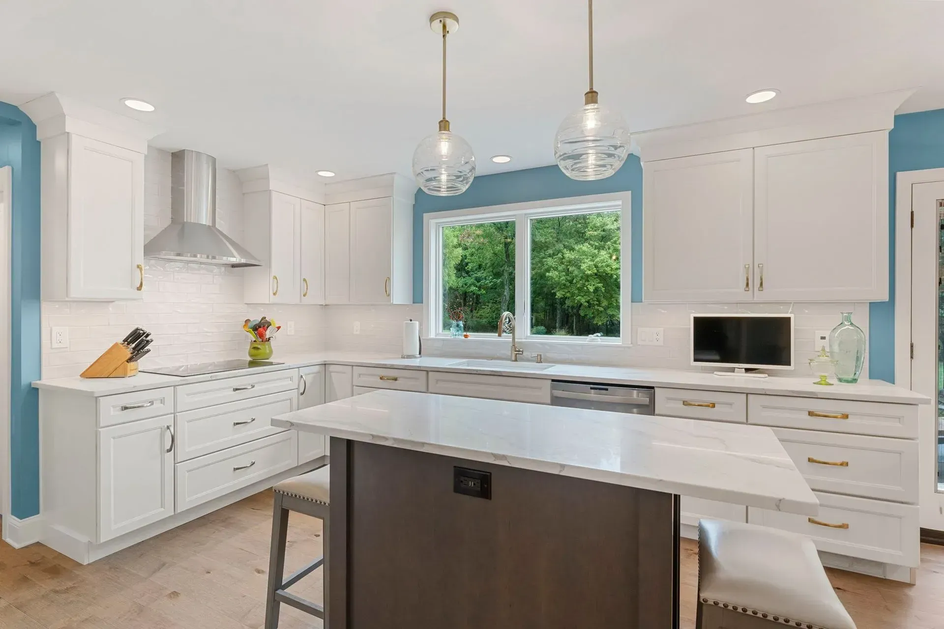 Bright modern white kitchen with blue walls, island, pendant lights, and large window over the sink  In Bucks County PA