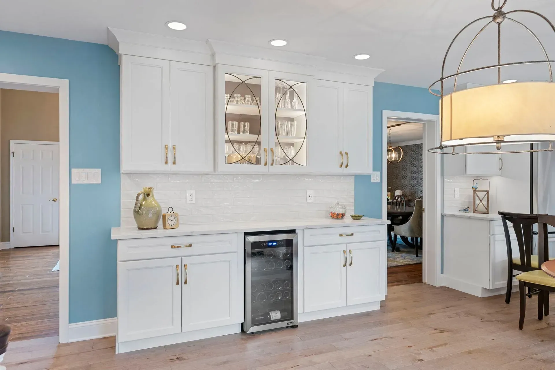 Bright white kitchen with light blue cabinets, island seating, wood floors, and a pendant light over a small desk area  In Bucks County PA