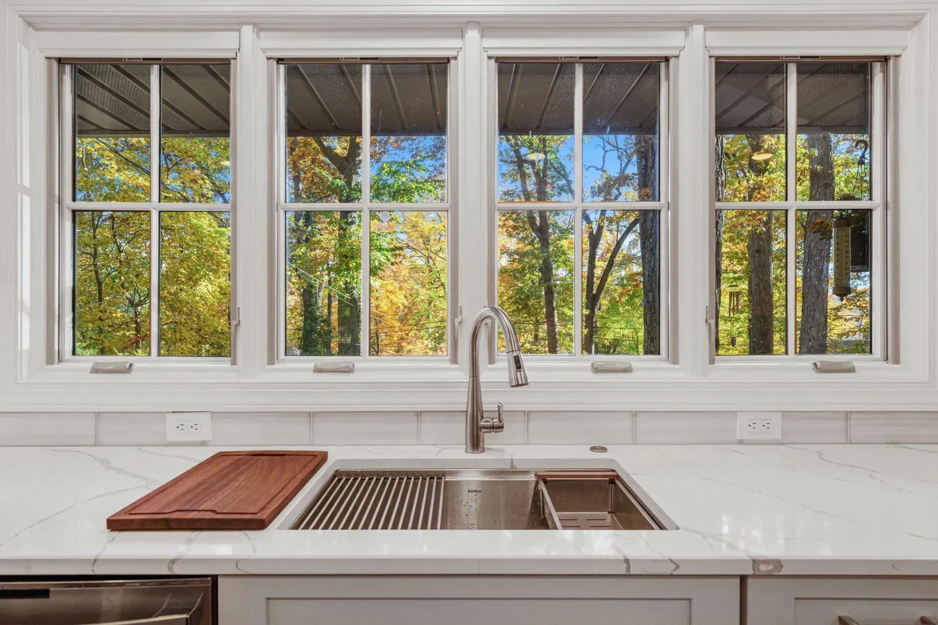 Bright kitchen window above a white countertop and sink, with a cutting board and trees outside in Bucks County PA