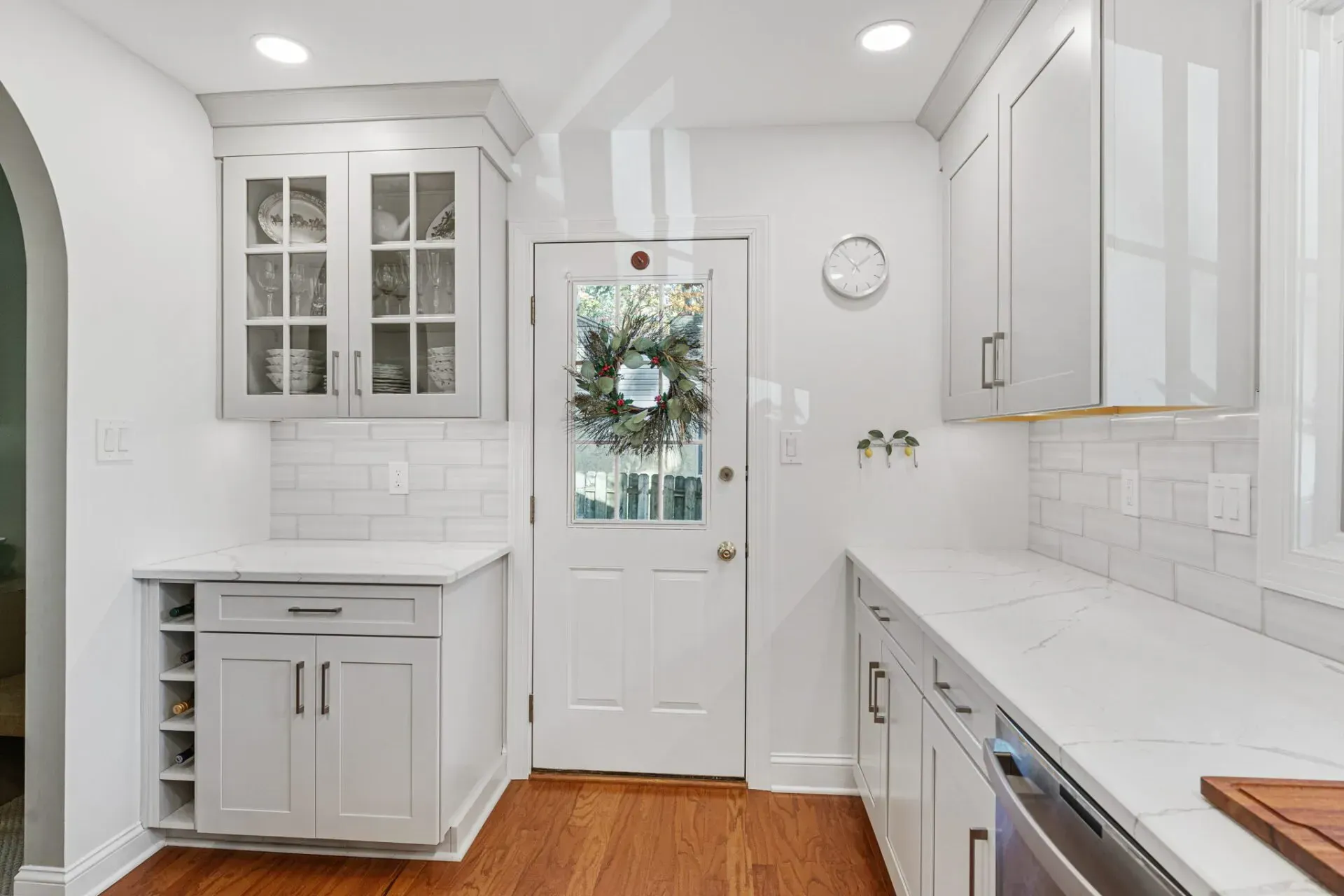 Bright white kitchen with cabinets, marble counters, wood floor, and a decorated back door in Bucks County PA
