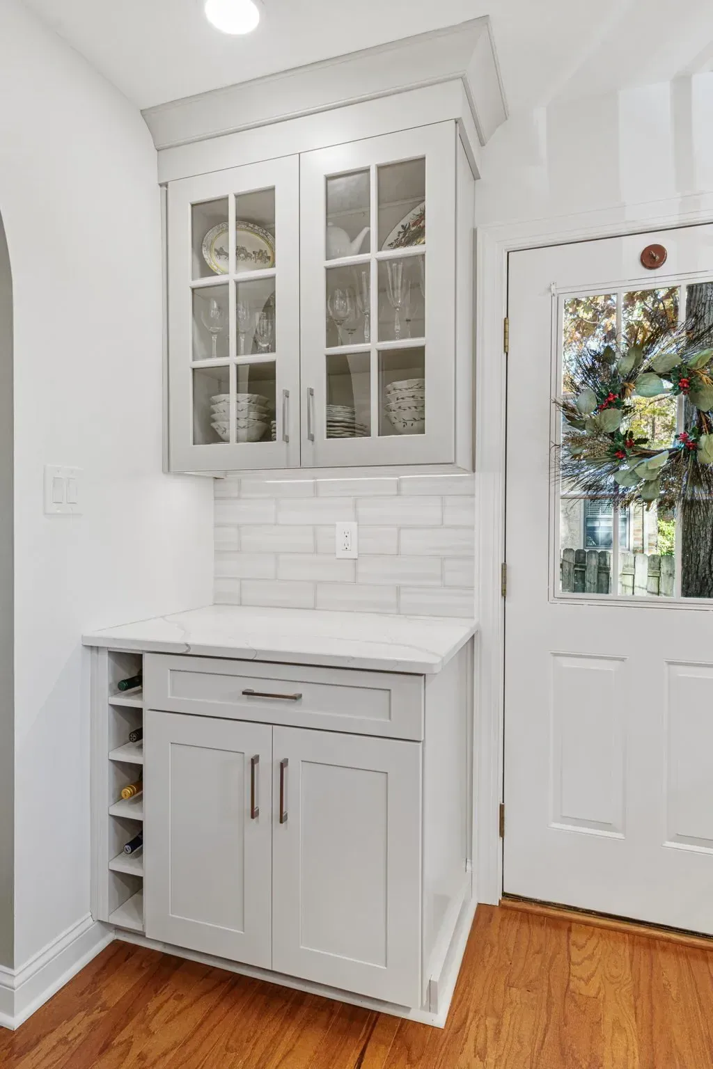 White kitchen nook with built-in cabinet, glass-front upper cabinets, and a decorative wreath on the door in Bucks County PA