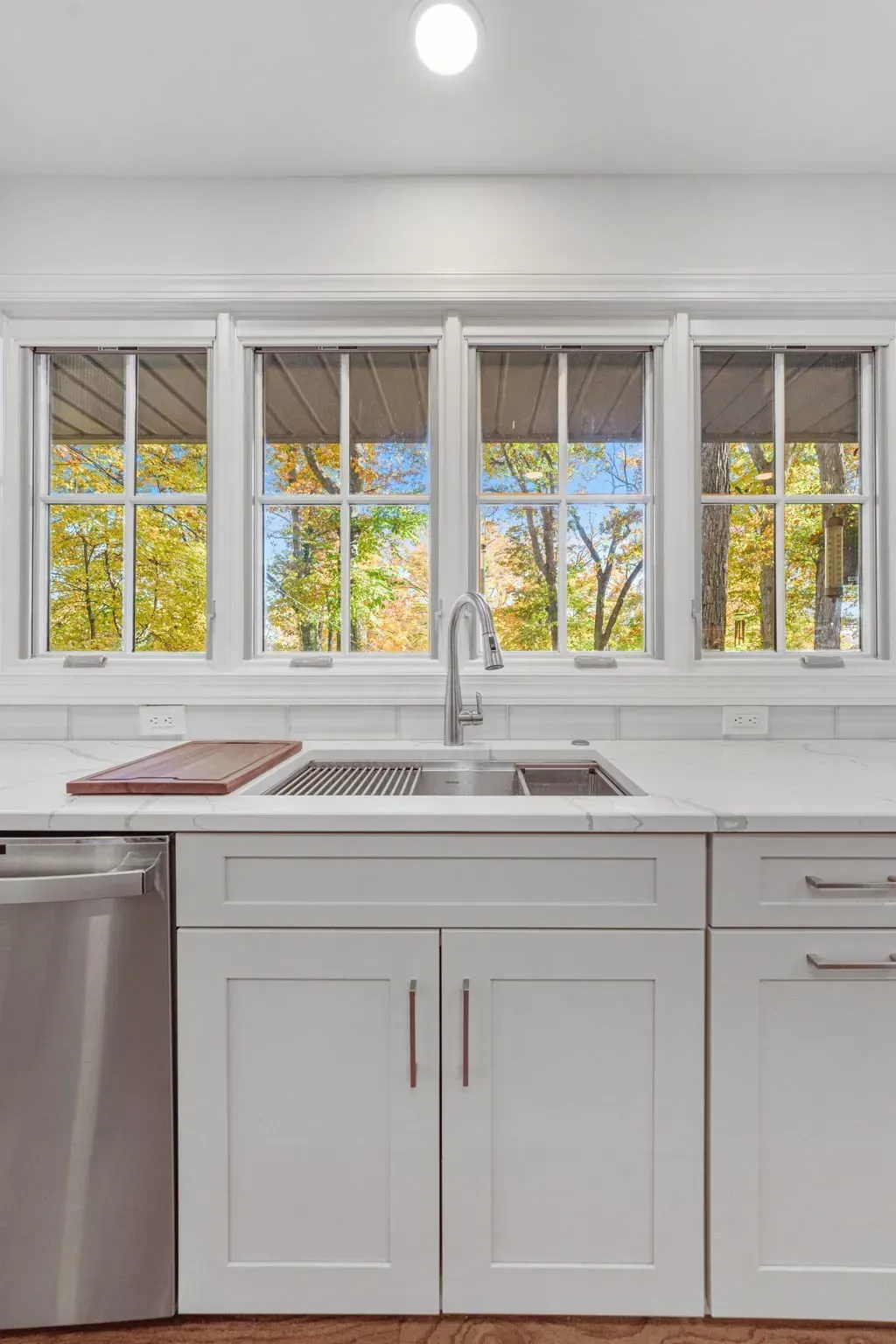 Bright modern kitchen with white cabinets, sink, and windows overlooking autumn trees in Bucks County PA