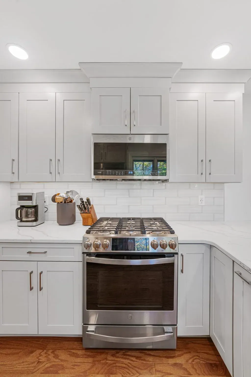 Bright white kitchen with stainless steel stove, microwave, cabinets, and white subway tile backsplash  in Bucks County PA