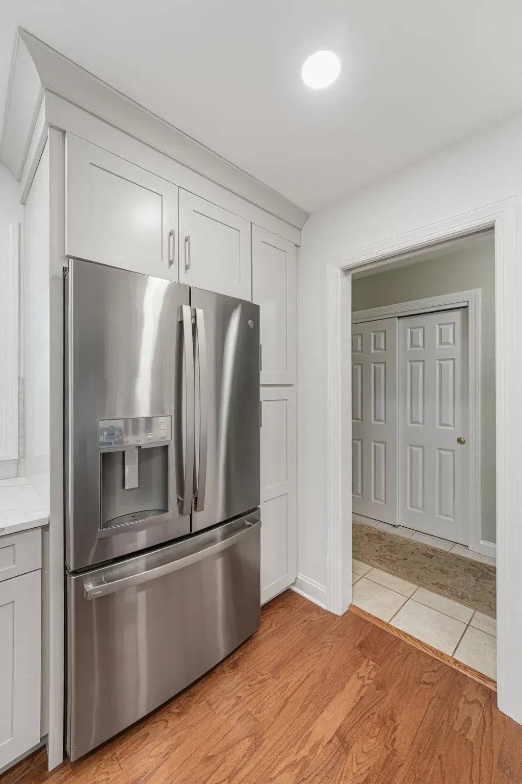 Modern kitchen with stainless steel refrigerator, white cabinets, and hardwood floor leading to a tiled entryway  in Bucks County PA