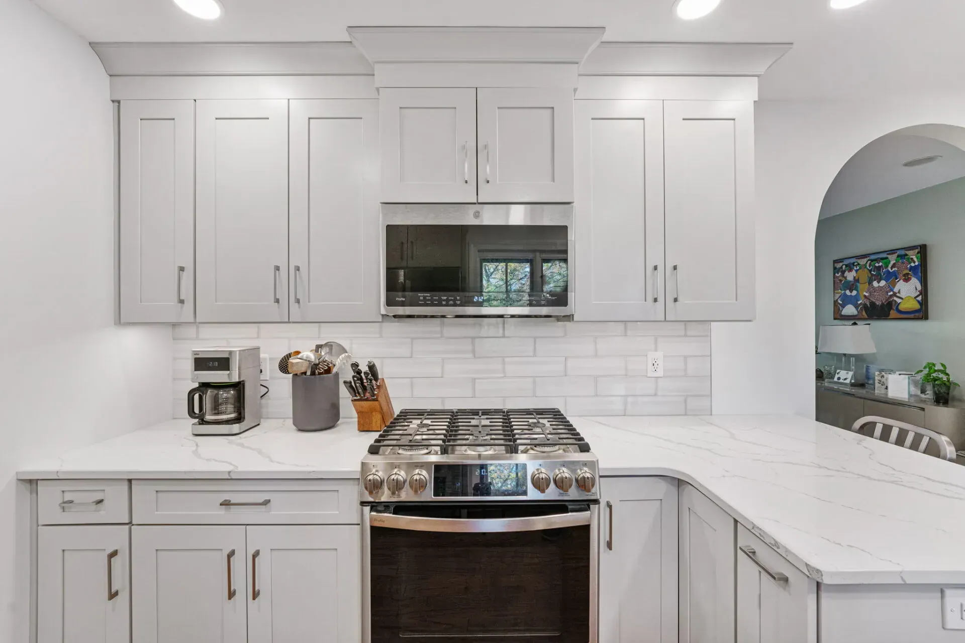 Bright white kitchen with gas range, subway tile backsplash, and a large arched opening to a living room in Bucks County PA