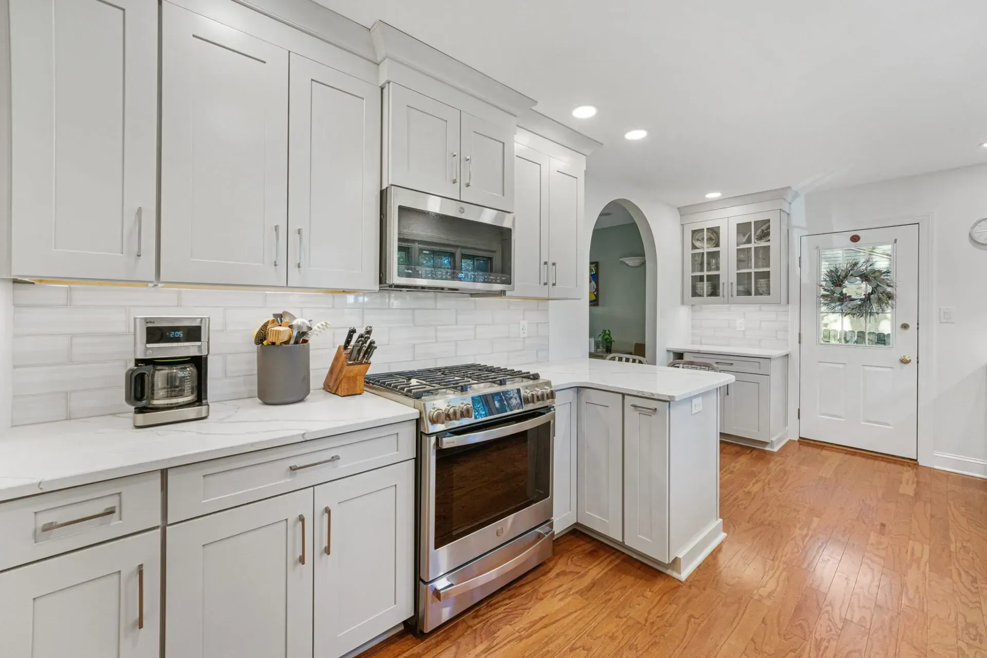 Bright white modern kitchen with stainless steel stove, marble island, and hardwood floors in Bucks County PA