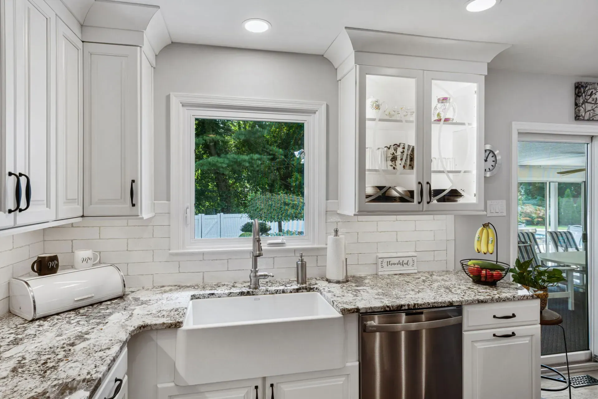 Bright white kitchen with farmhouse sink, granite counters, and a window above the sink facing greenery In Bucks County PA