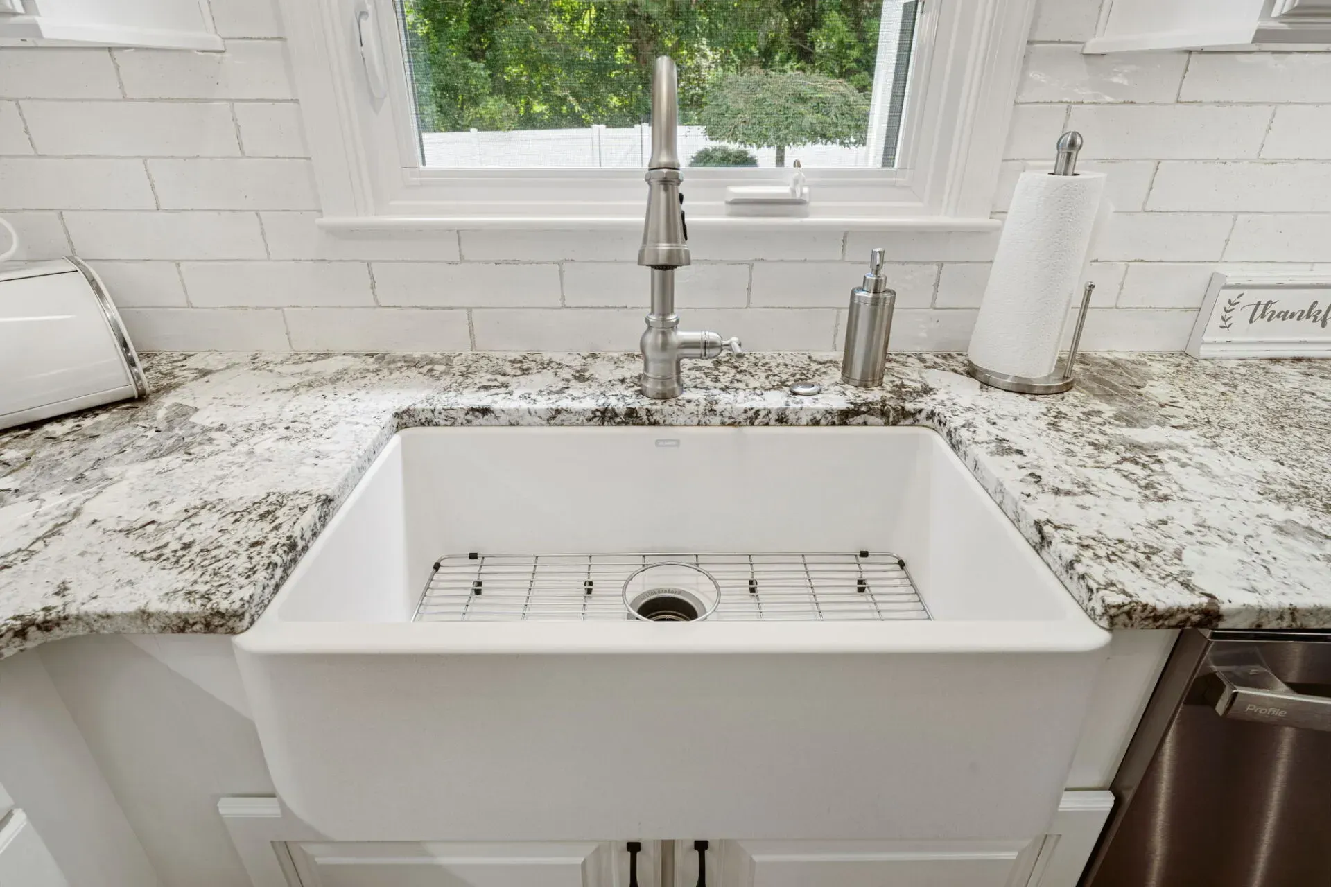 White farmhouse kitchen sink with granite countertop, chrome faucet, and window above the sink In Bucks County PA