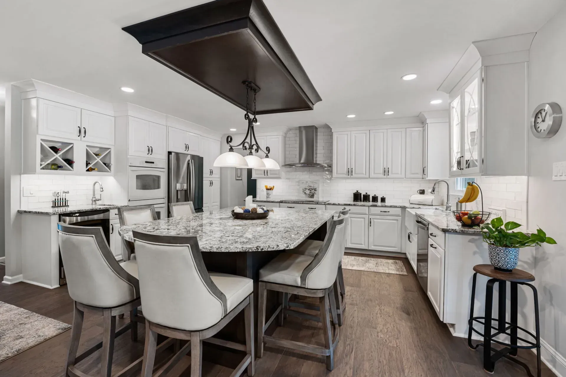 Bright white kitchen with granite island, barstools, pendant lights, and dark wood floor In Bucks Country PA