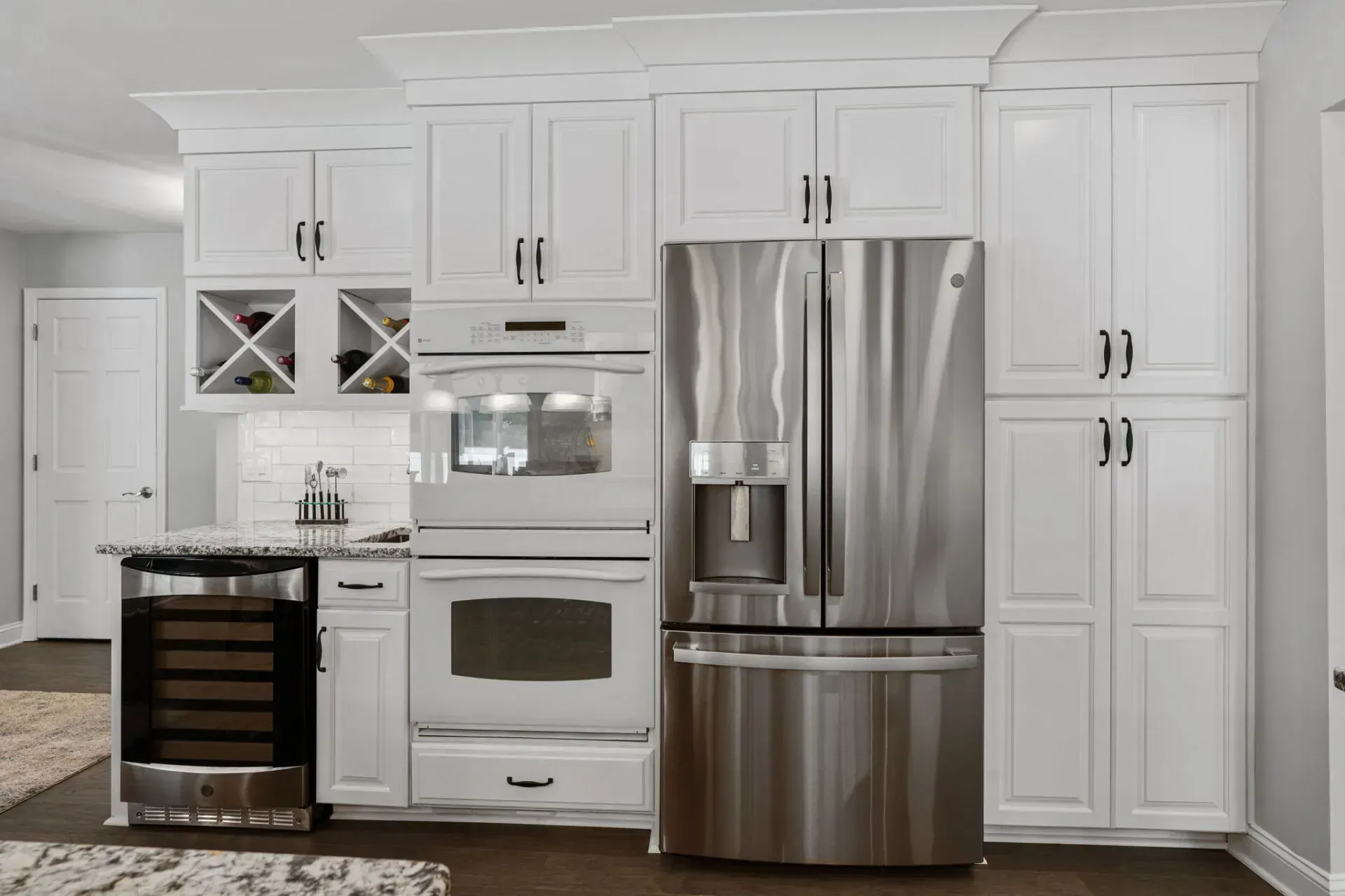 White kitchen with stainless steel fridge, oven, and wine cooler, featuring white cabinets and a dark wood floor In Bucks County PA