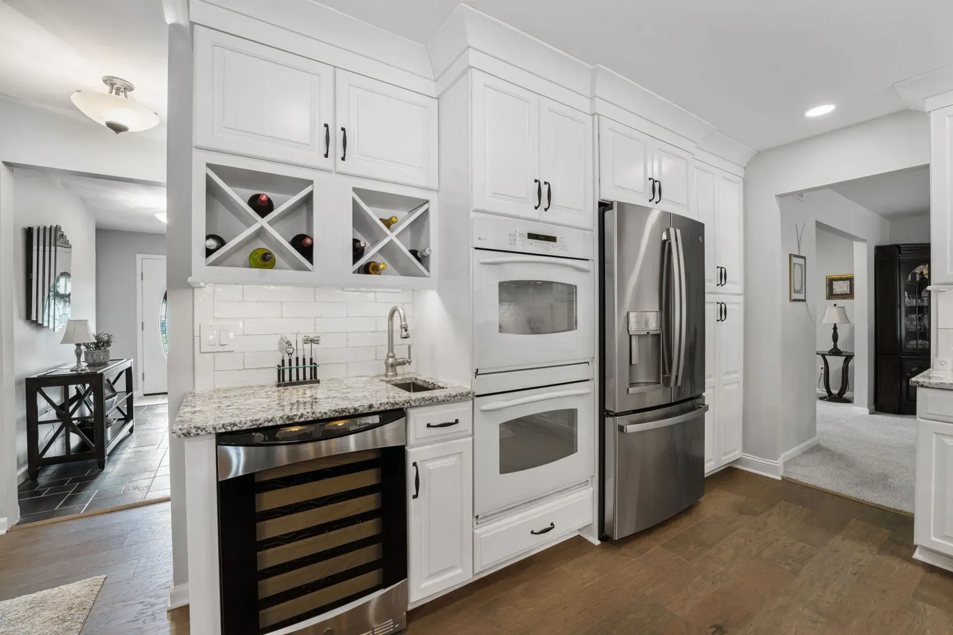 Bright white kitchen with stainless steel appliances, wine cooler, and marble countertops in an open home interior In Bucks County PA
