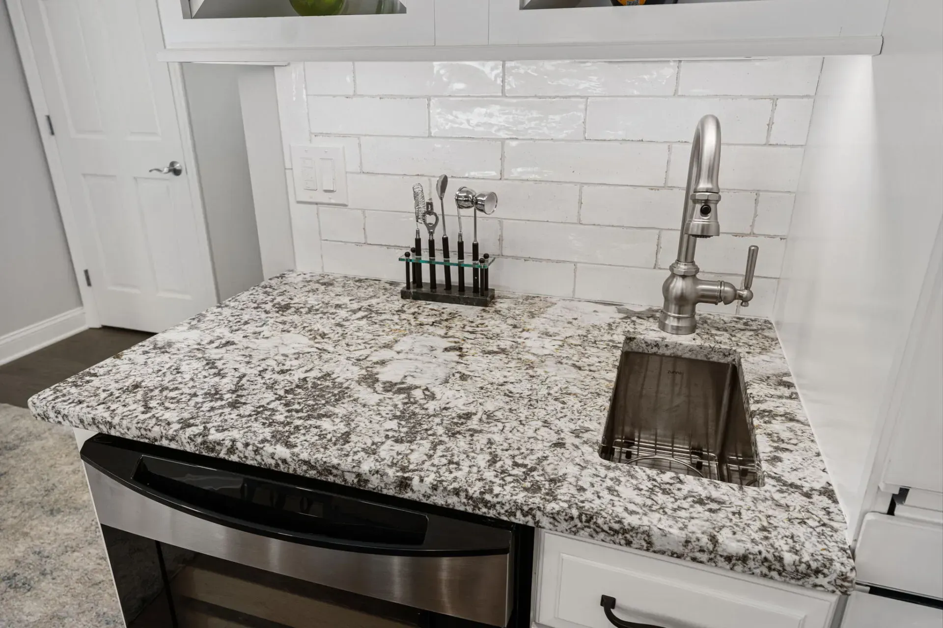 Granite kitchen countertop with sink, chrome faucet, and spice rack against white tile backsplash In Bucks County PA