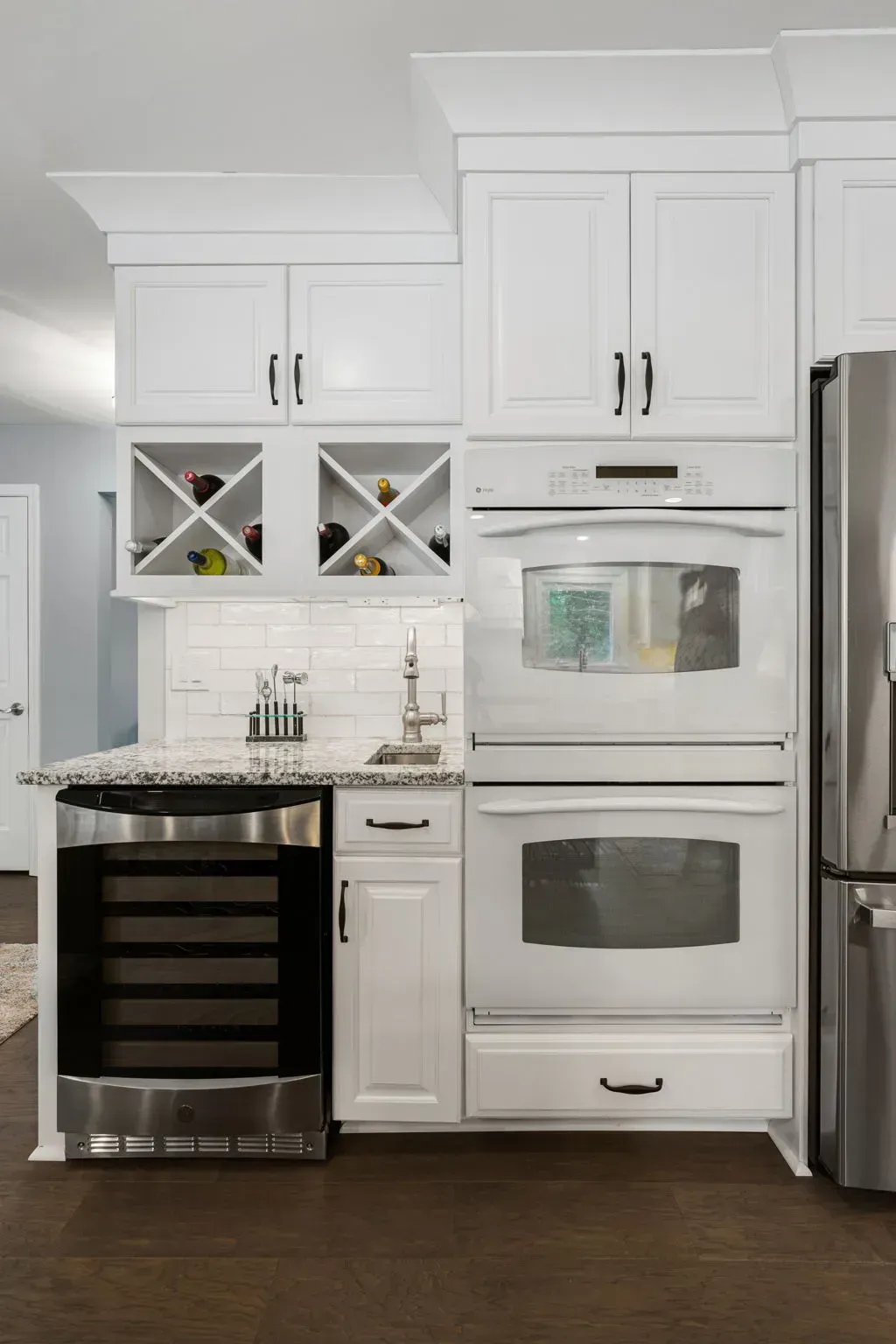 White kitchen with built-in wine cooler, double oven, and stainless refrigerator beside marble countertop In Bucks County PA