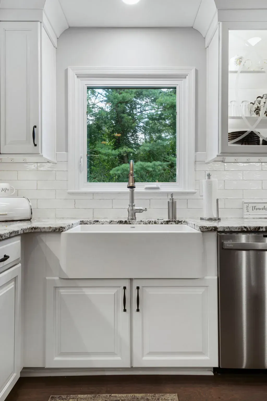 Bright white kitchen sink under a window with green trees outside and stainless steel dishwasher nearby In Bucks County PA