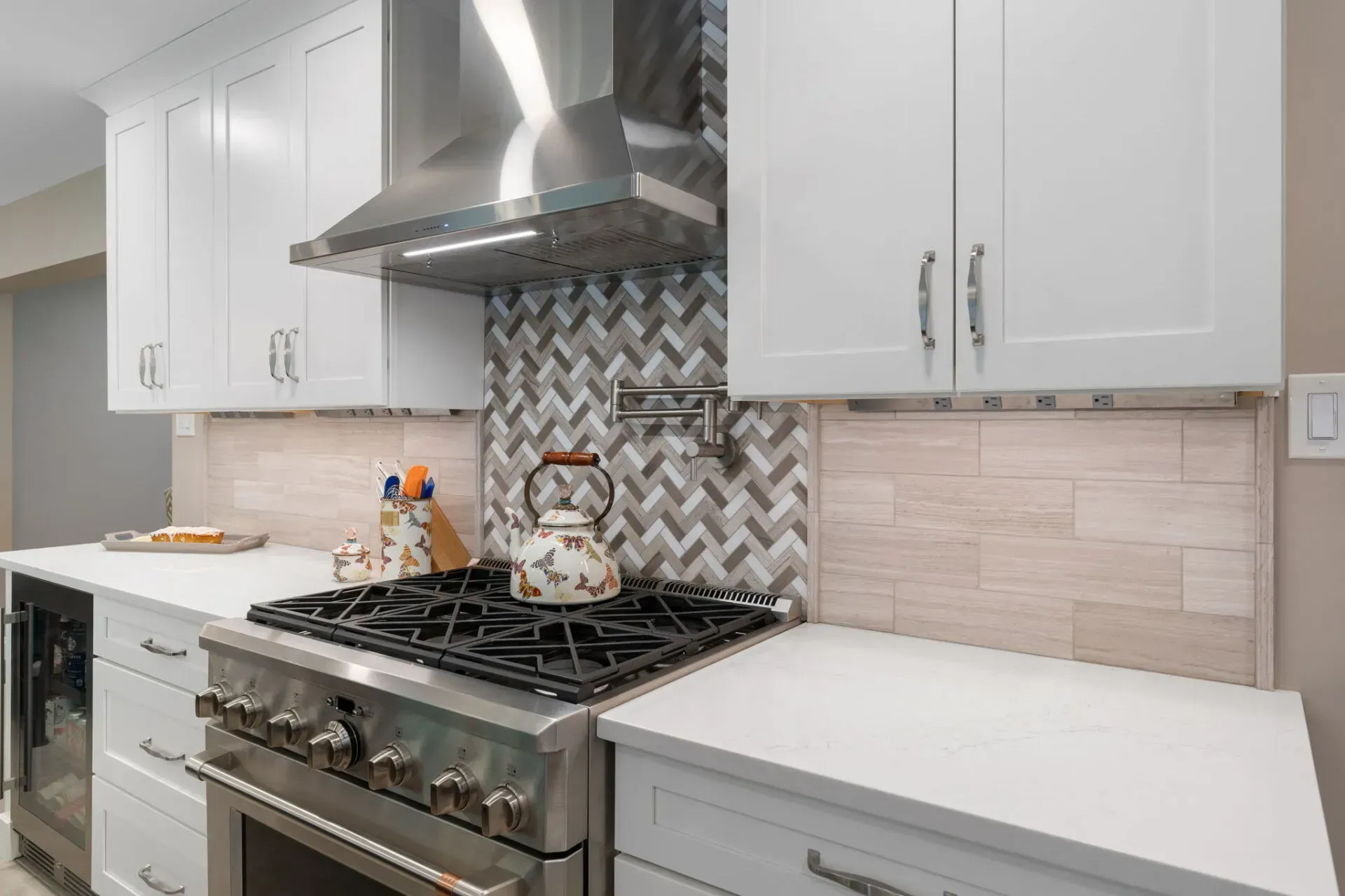 Modern white kitchen with stainless steel stove, range hood, and patterned backsplash In Bucks County PA