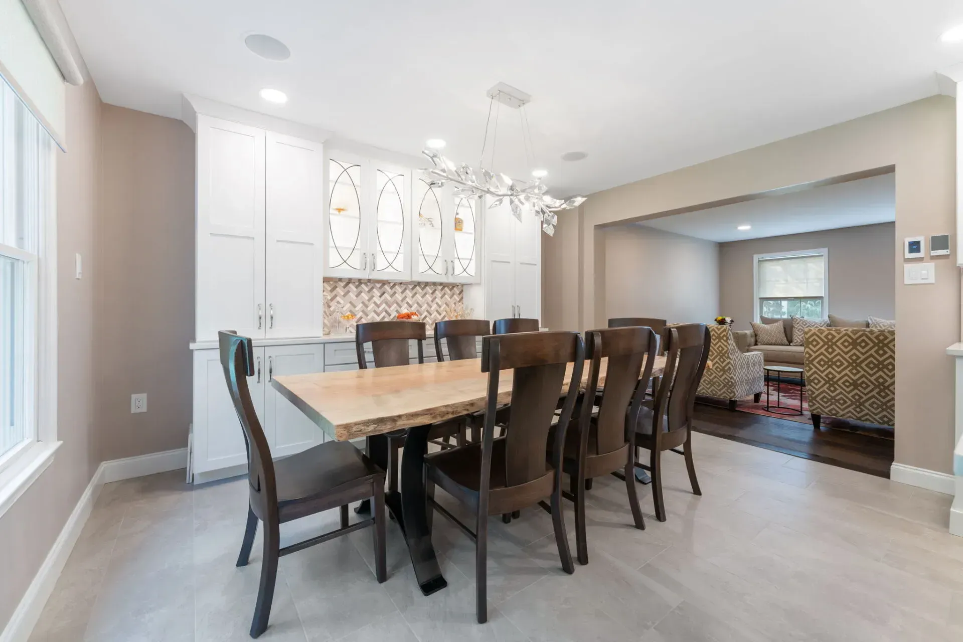 Bright dining room with a long wooden table, dark chairs, and a chandelier, opening to a living room In Bucks County PA