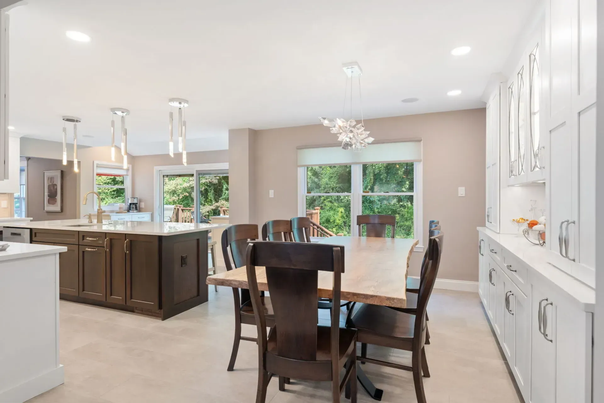 Open-concept kitchen and dining area with dark wood table, island, and large windows overlooking greenery In Bucks County PA