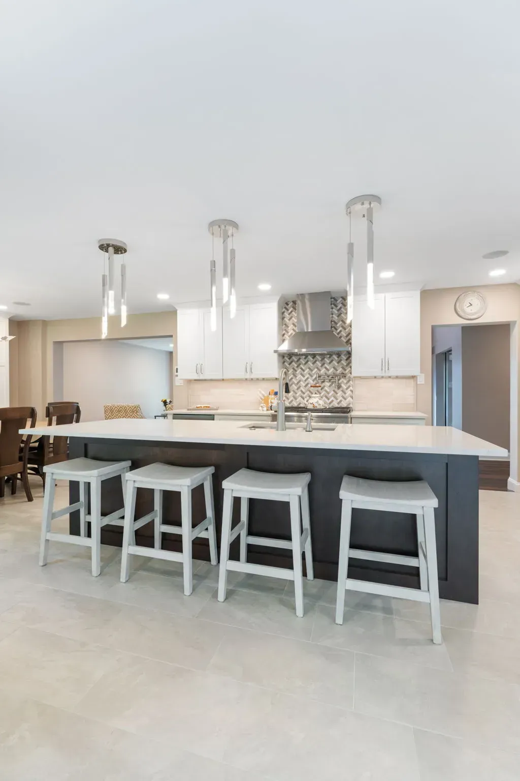 Modern kitchen with white island, gray stools, pendant lights, and tiled backsplash In Bucks County PA