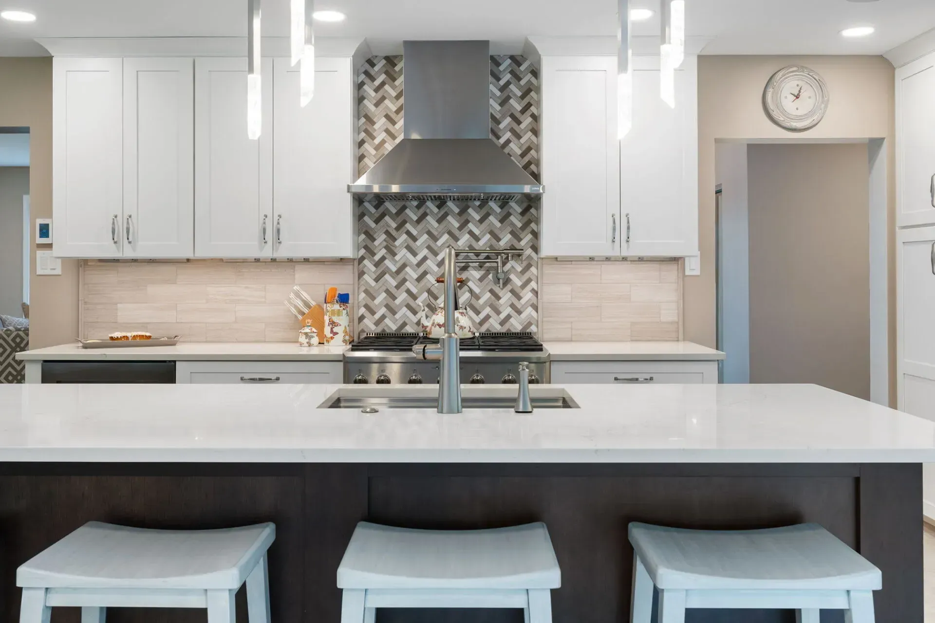 Modern white kitchen with island, stainless range hood, and three stools under a wall clock In Bucks County PA