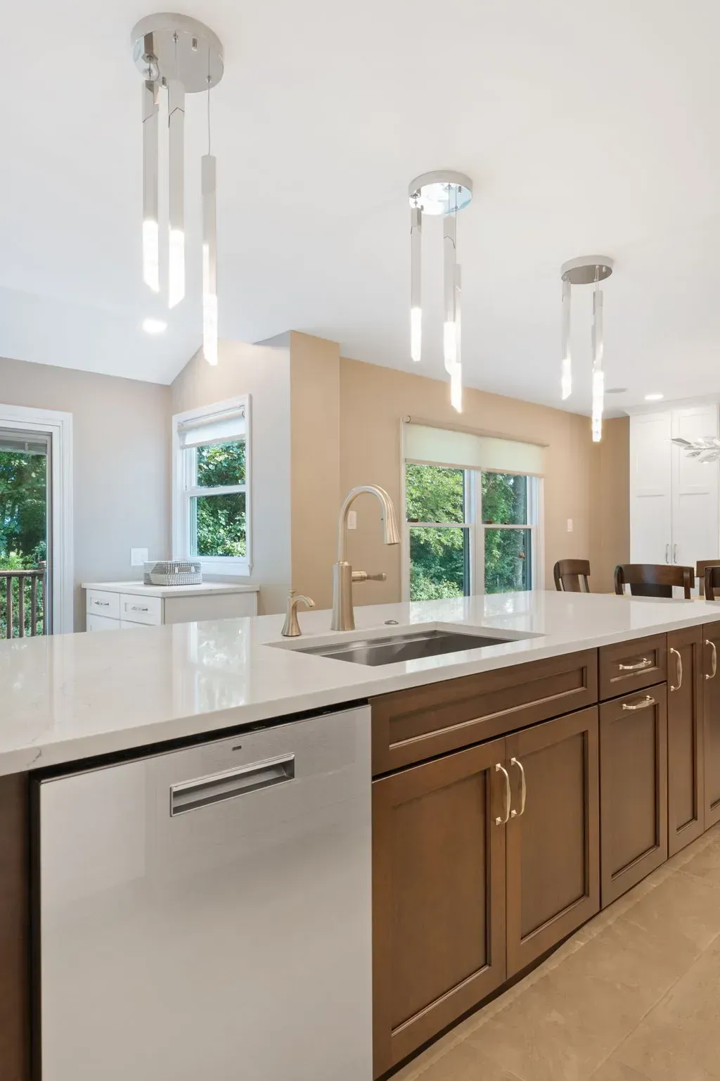 Modern kitchen with white island, wood cabinets, pendant lights, and large windows In Bucks County PA